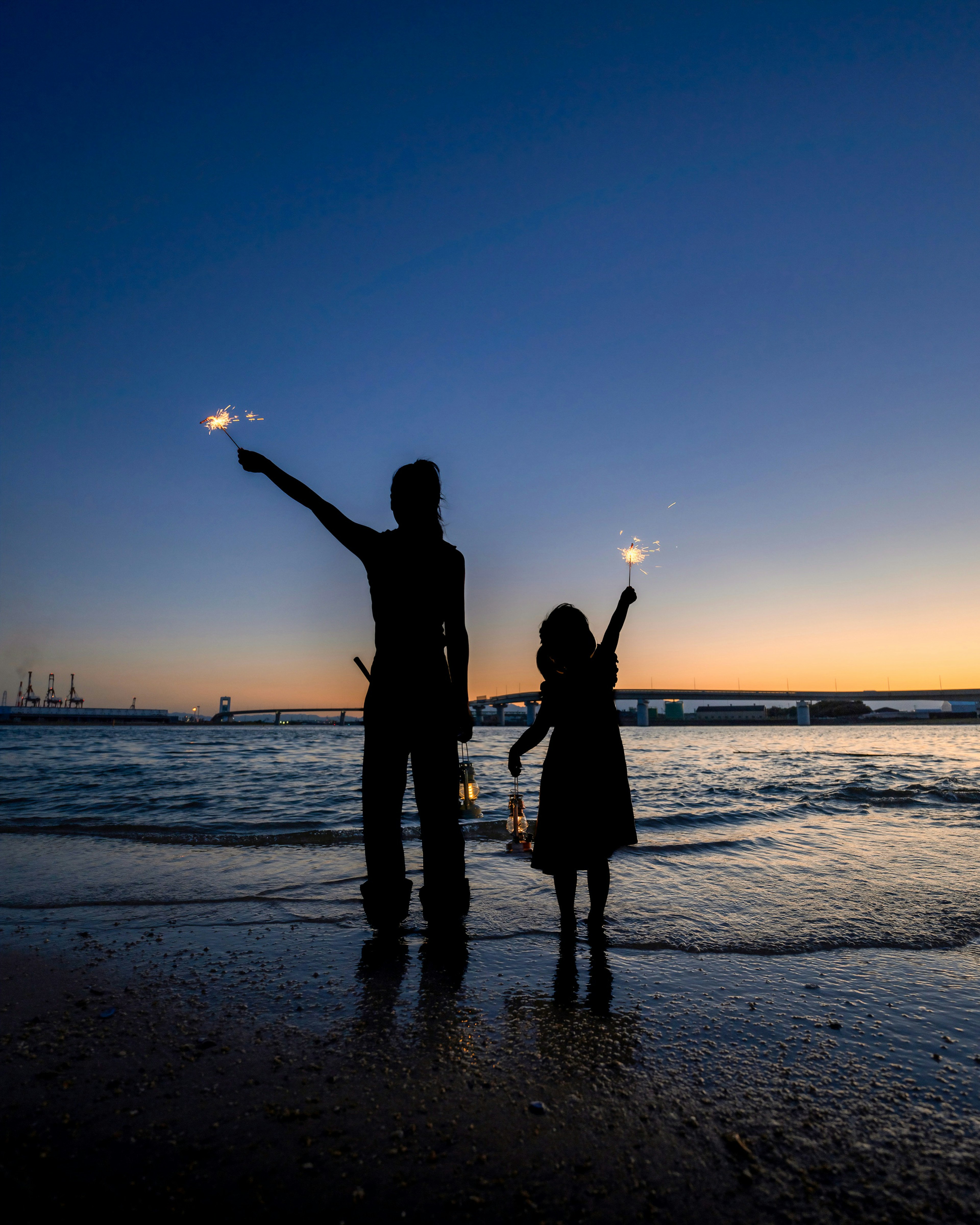 Silhouette of a parent and child holding sparklers on a beach at sunset