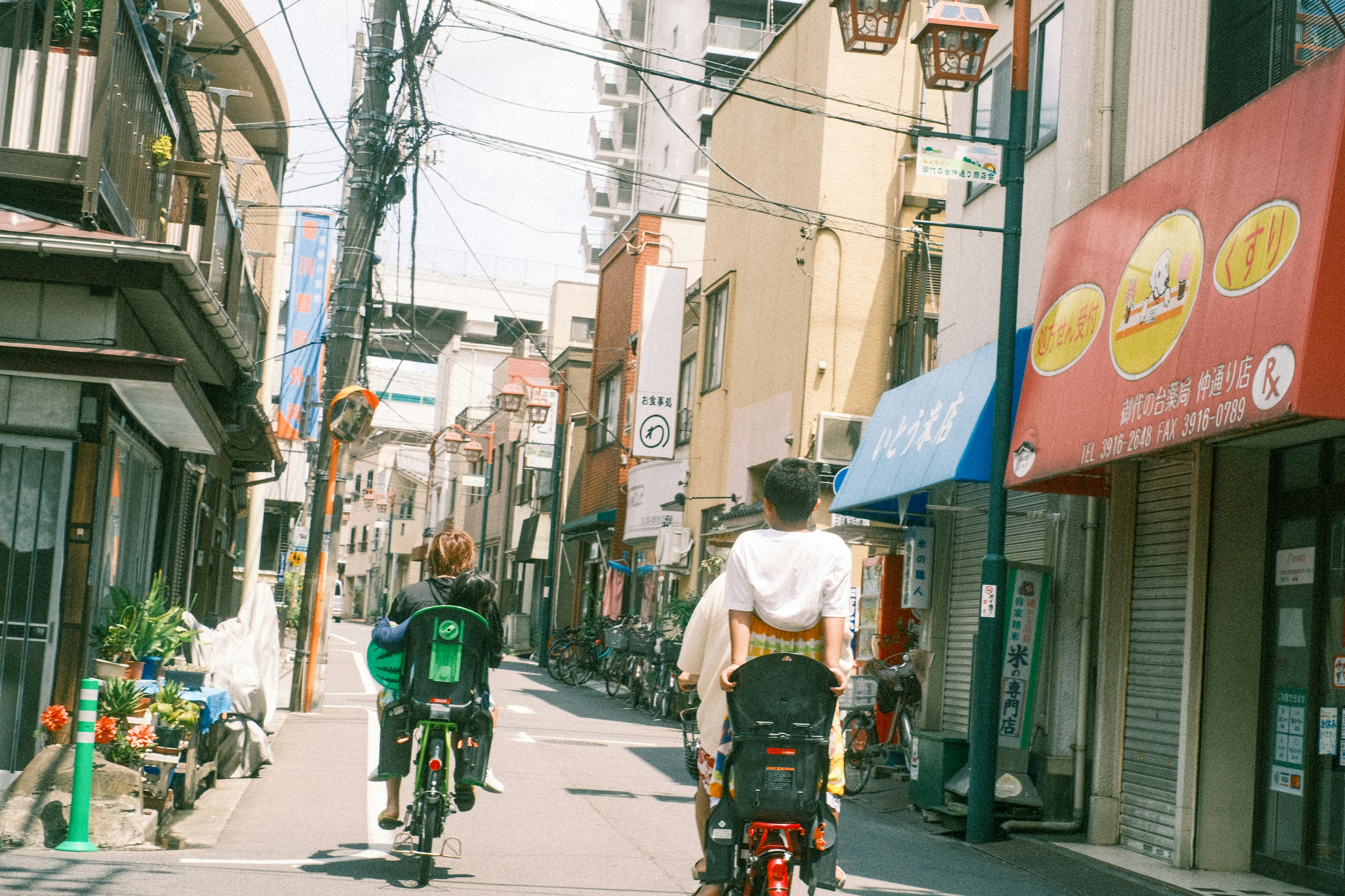 自転車に乗る二人が狭い通りを進む風景 古い建物と電線が見える