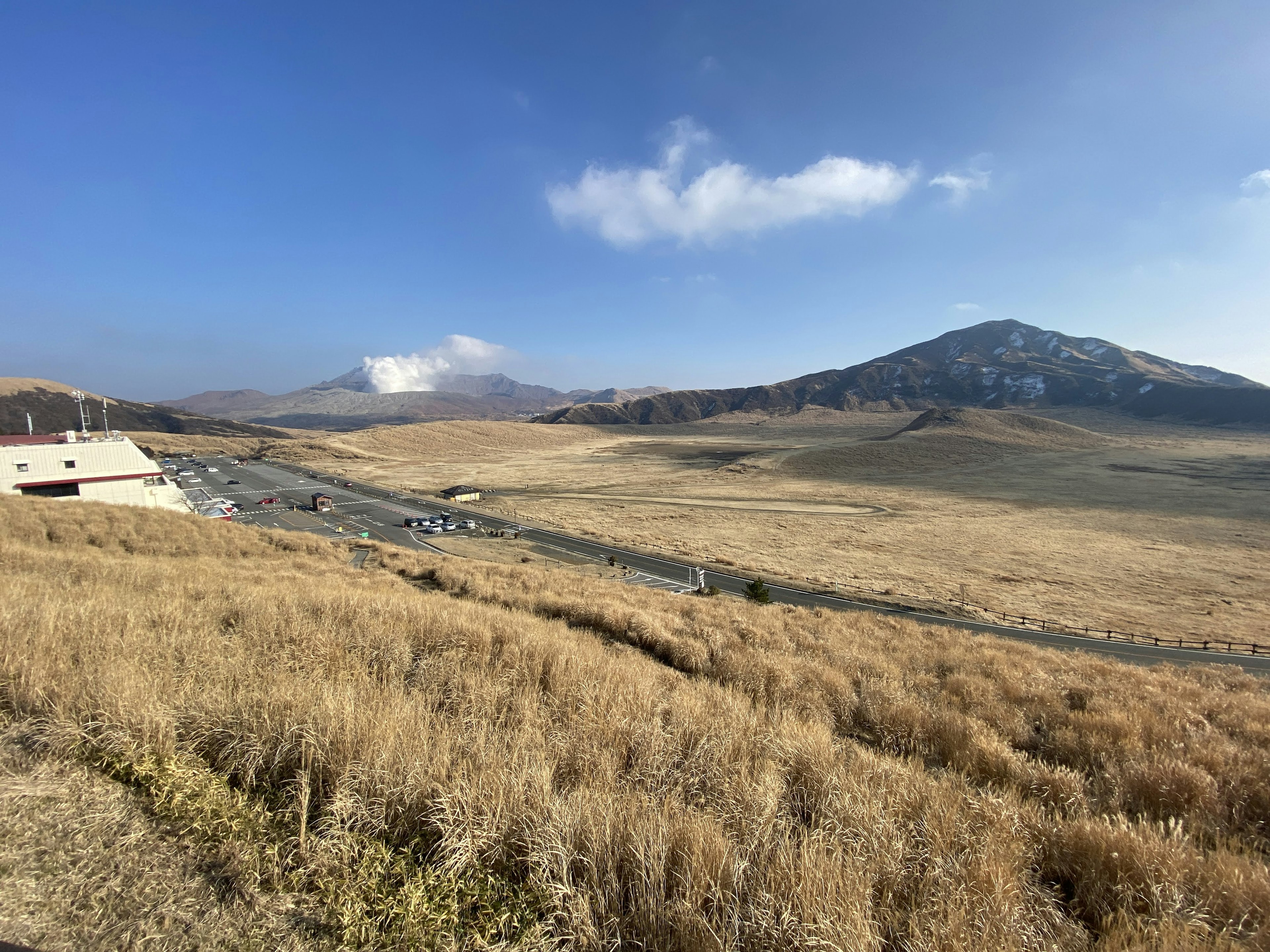 Vast grassland with mountains under a clear blue sky and clouds