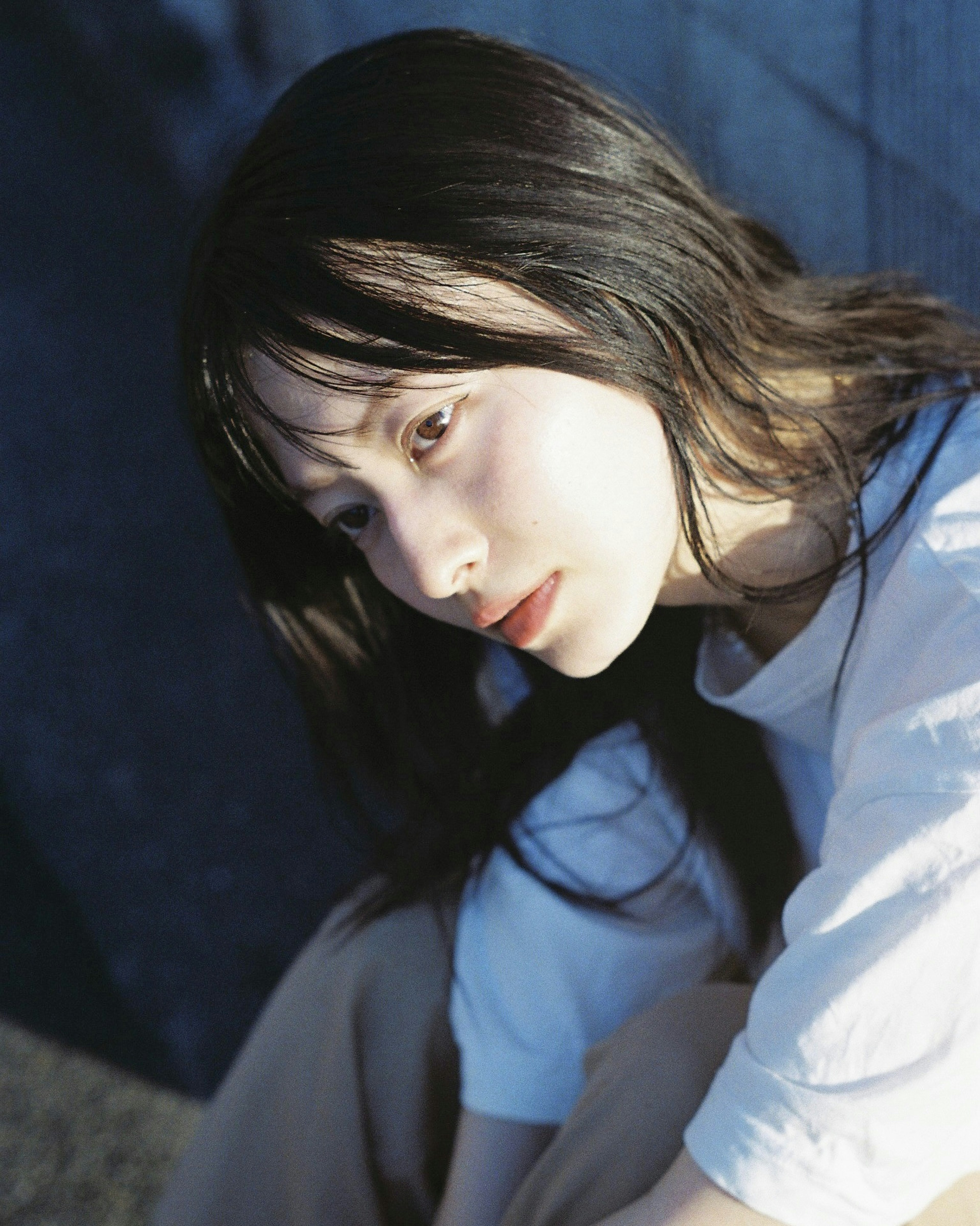 Portrait of a woman with long dark hair sitting against a blue background