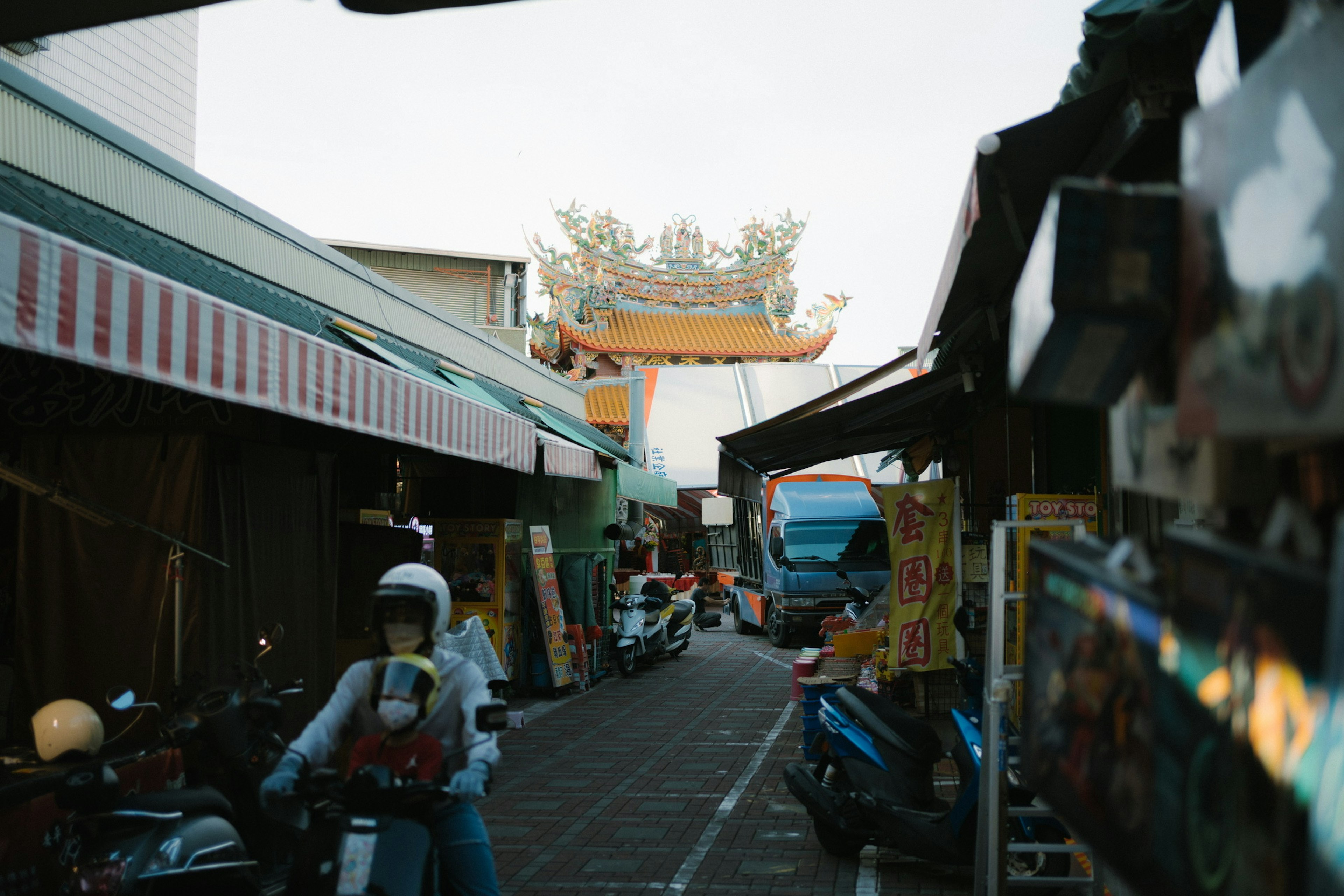 市場の路地にバイクが並び、遠くに寺の門が見える