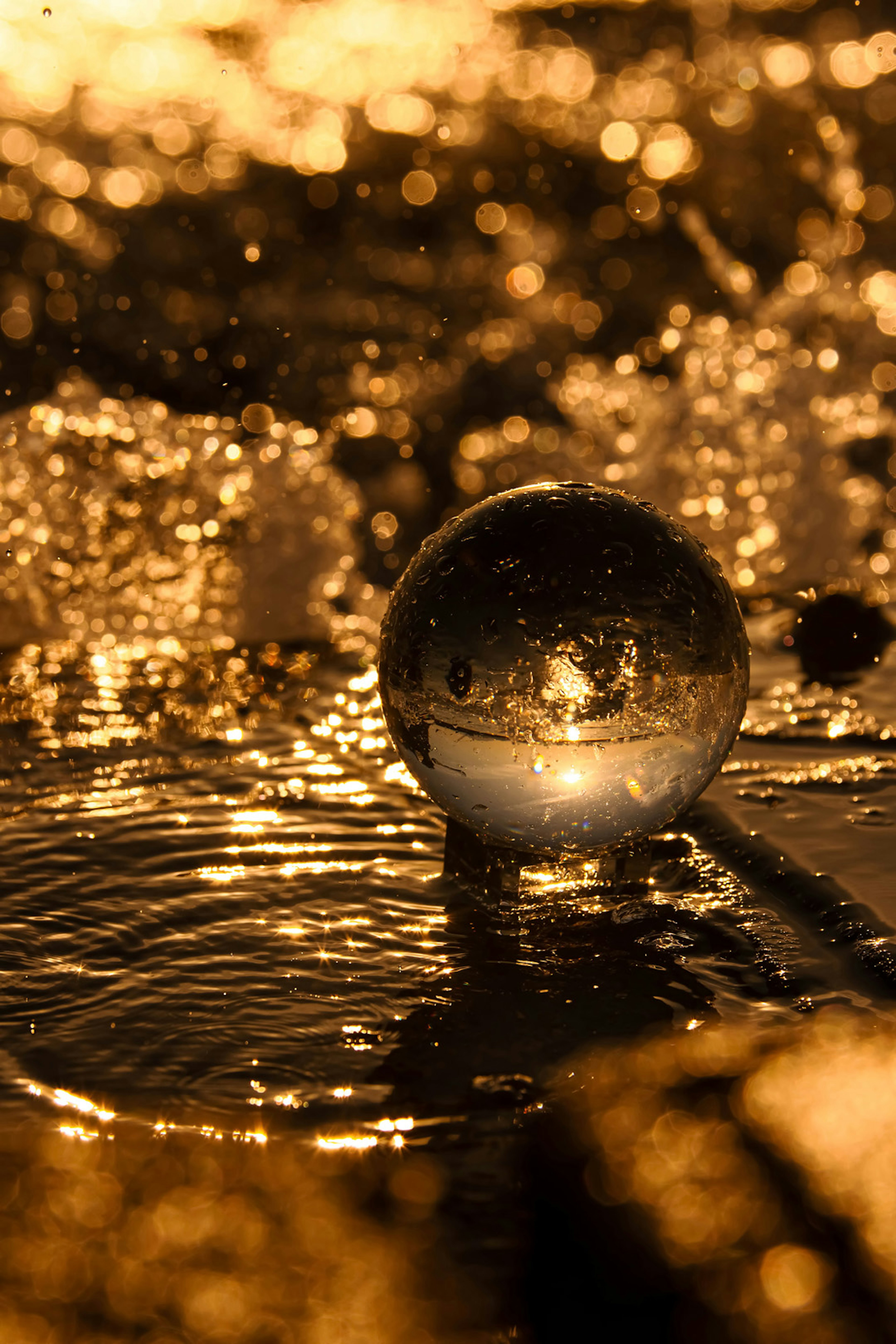 Transparent sphere resting on shimmering water with golden reflections