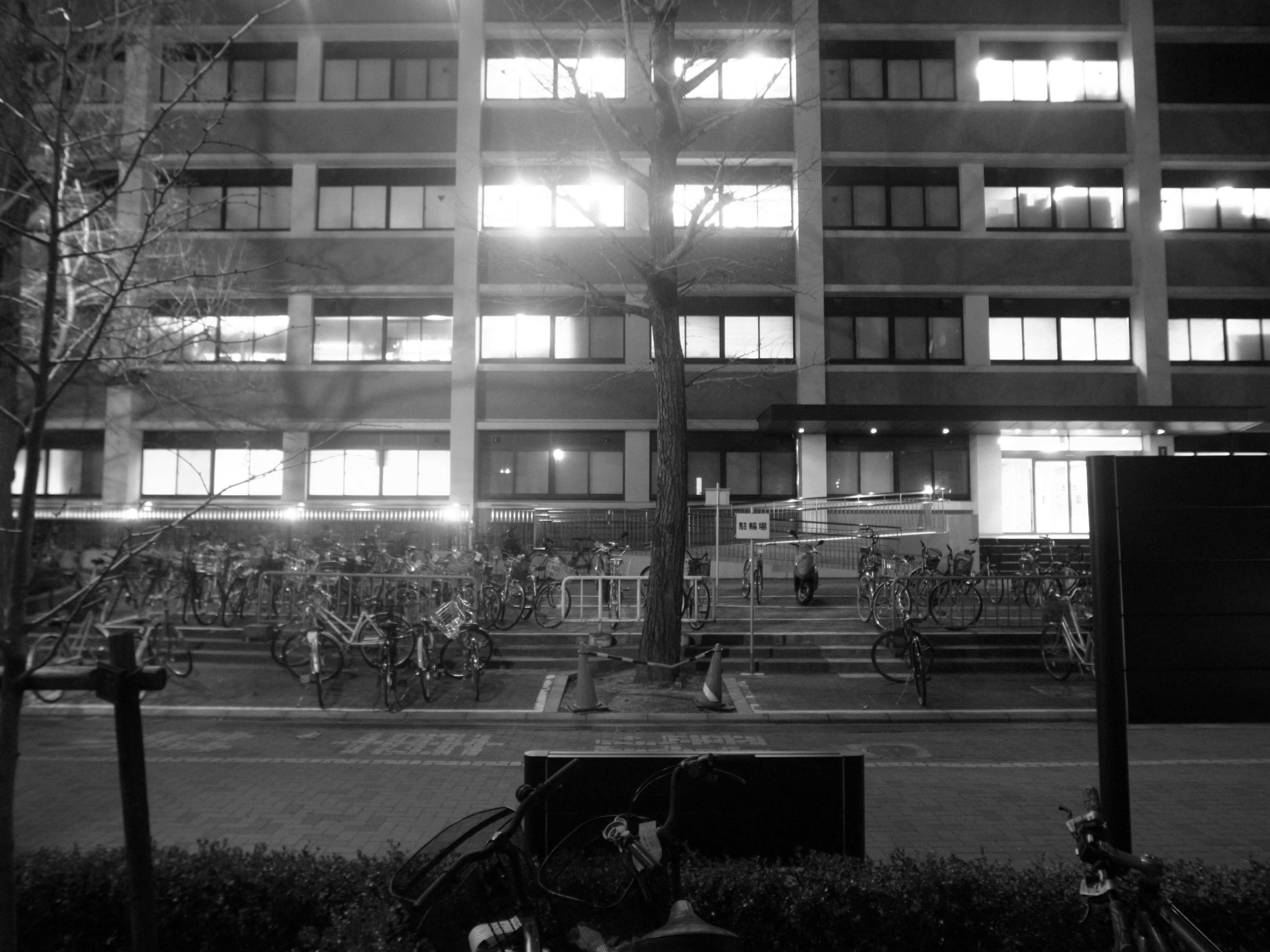 Night cityscape featuring a mid-rise building and people sitting on steps