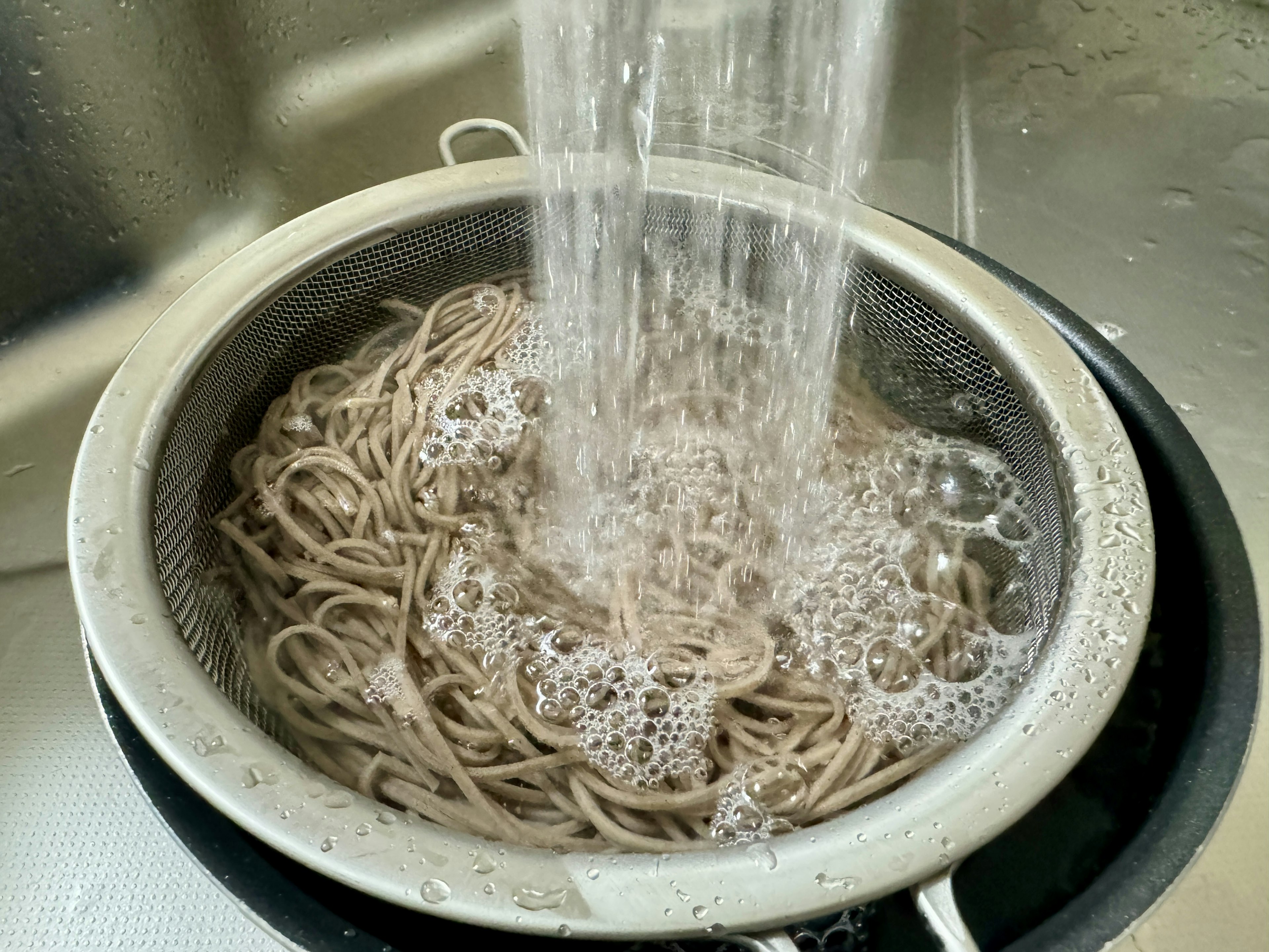 Soba noodles being rinsed under running water