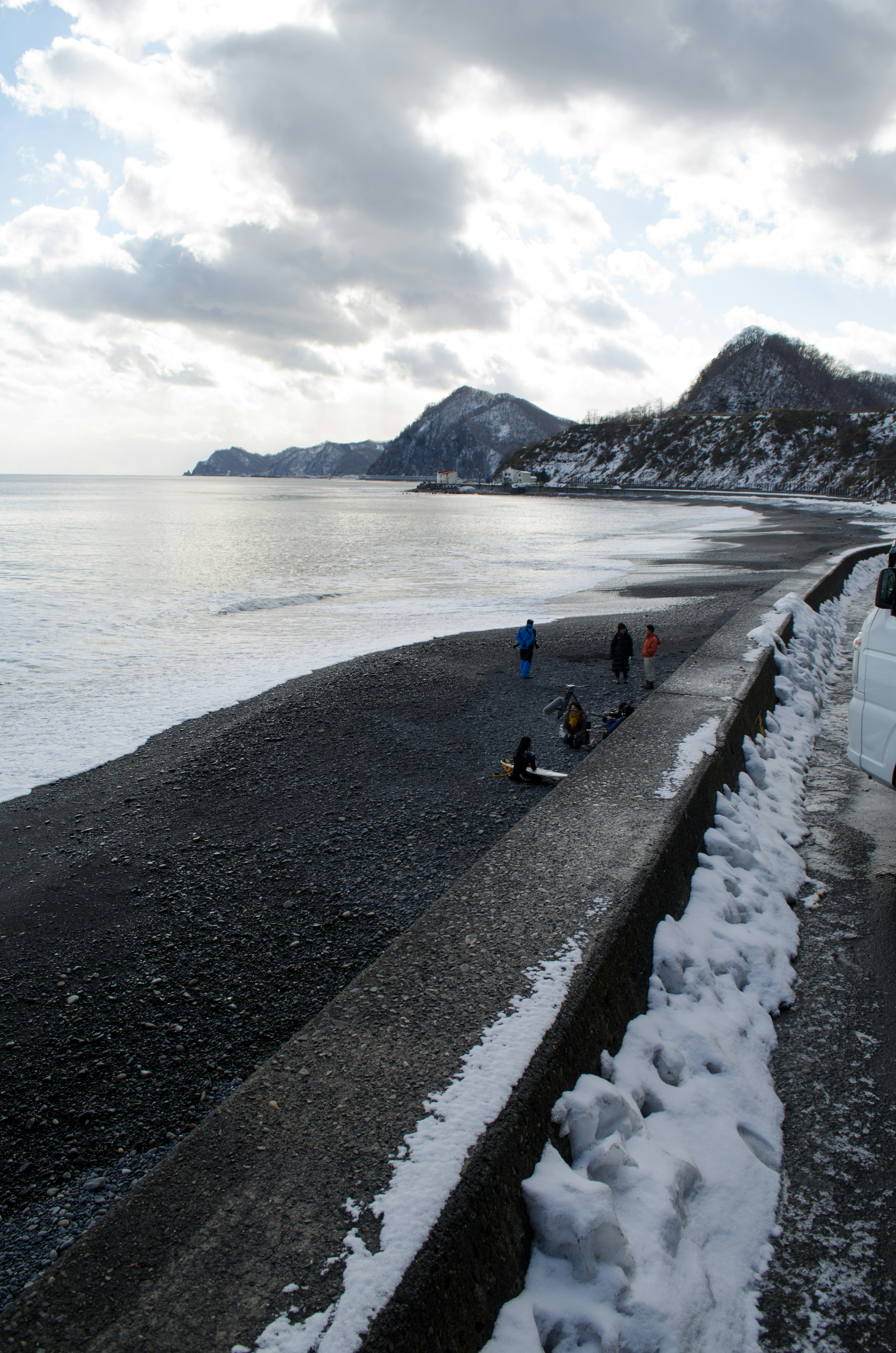 Des gens se promenant sur une plage enneigée avec des montagnes en arrière-plan