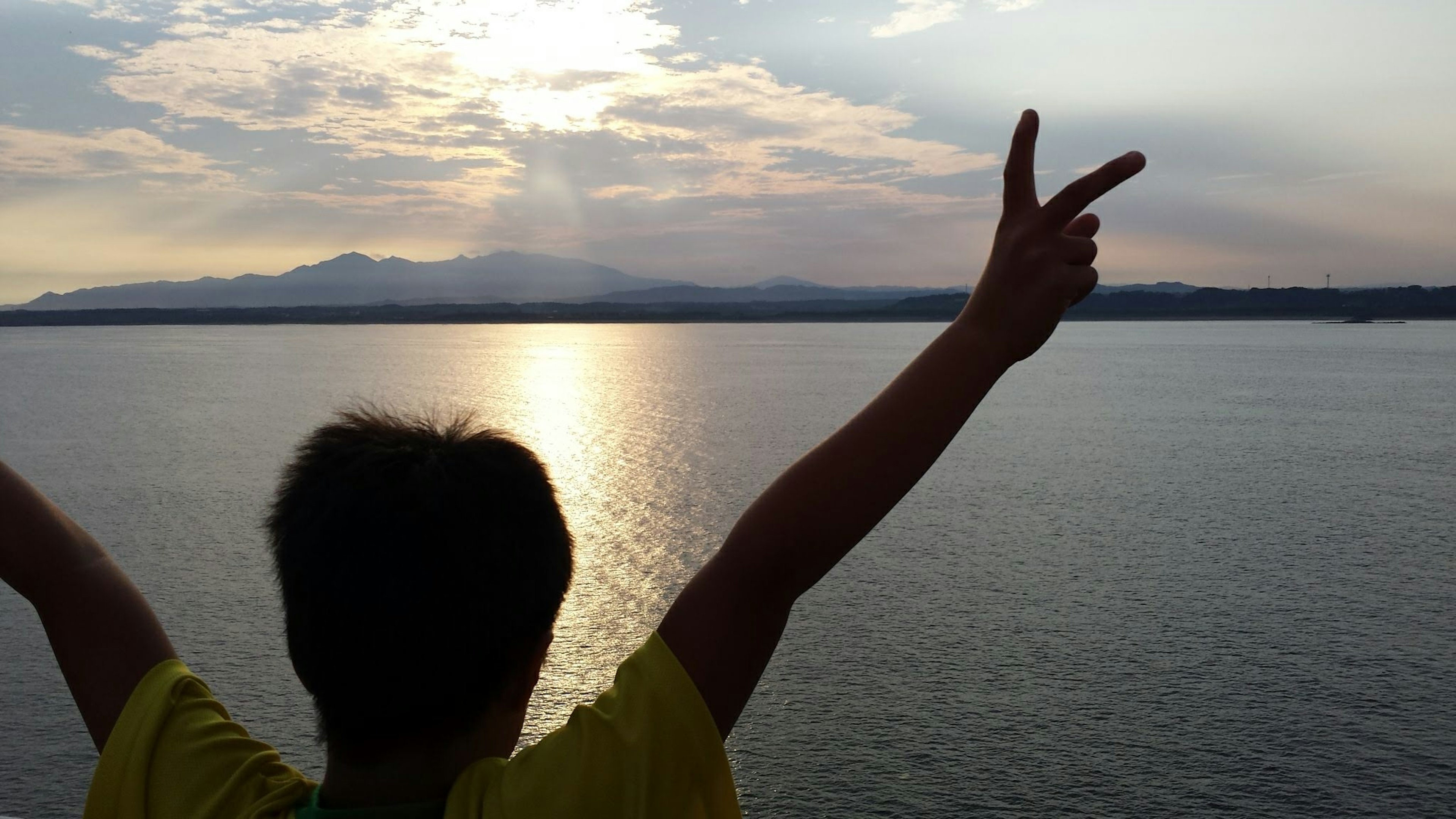 Silueta de un niño levantando las manos al atardecer