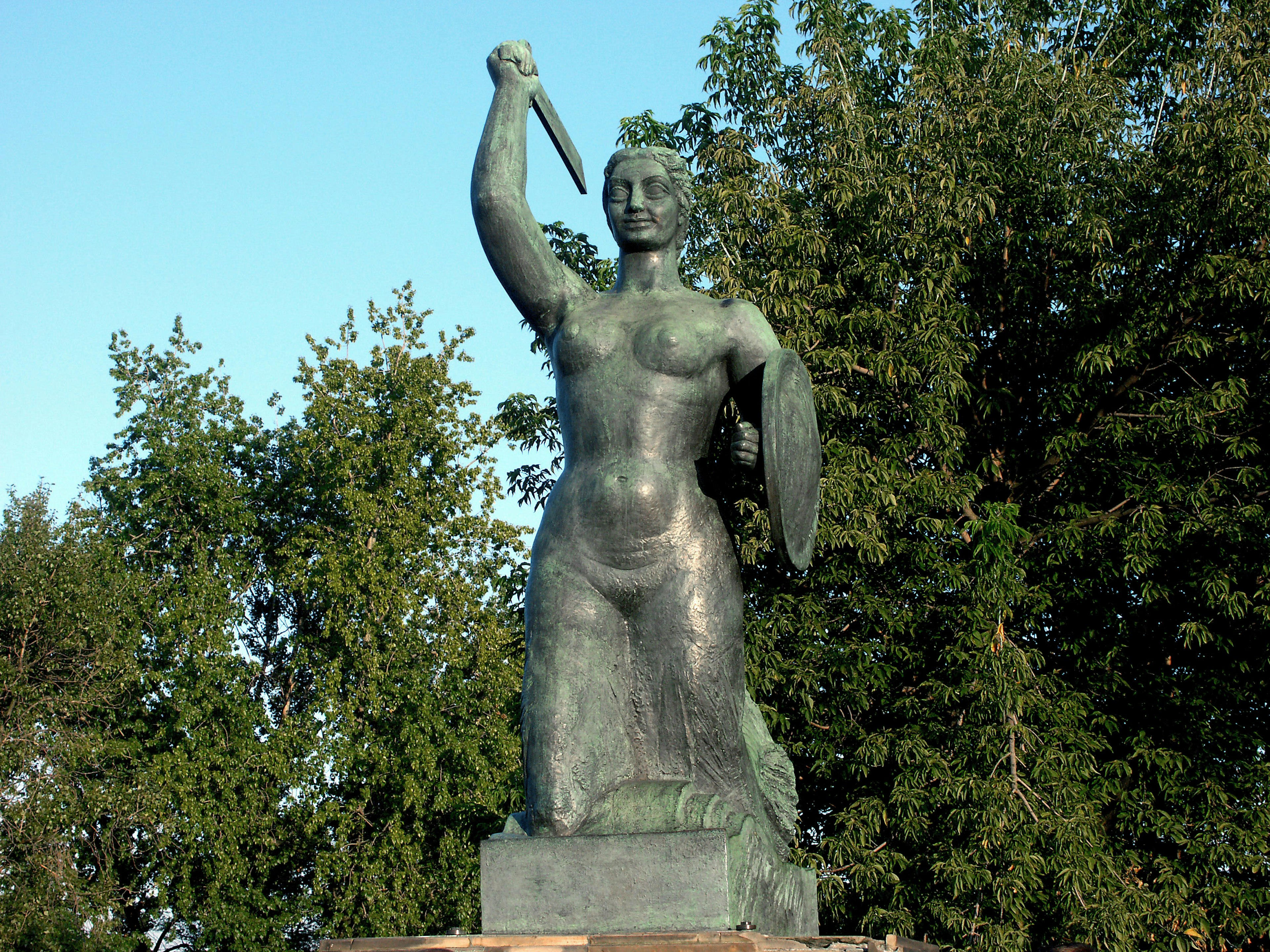 Une statue féminine courageuse tenant une épée entourée d'arbres verts