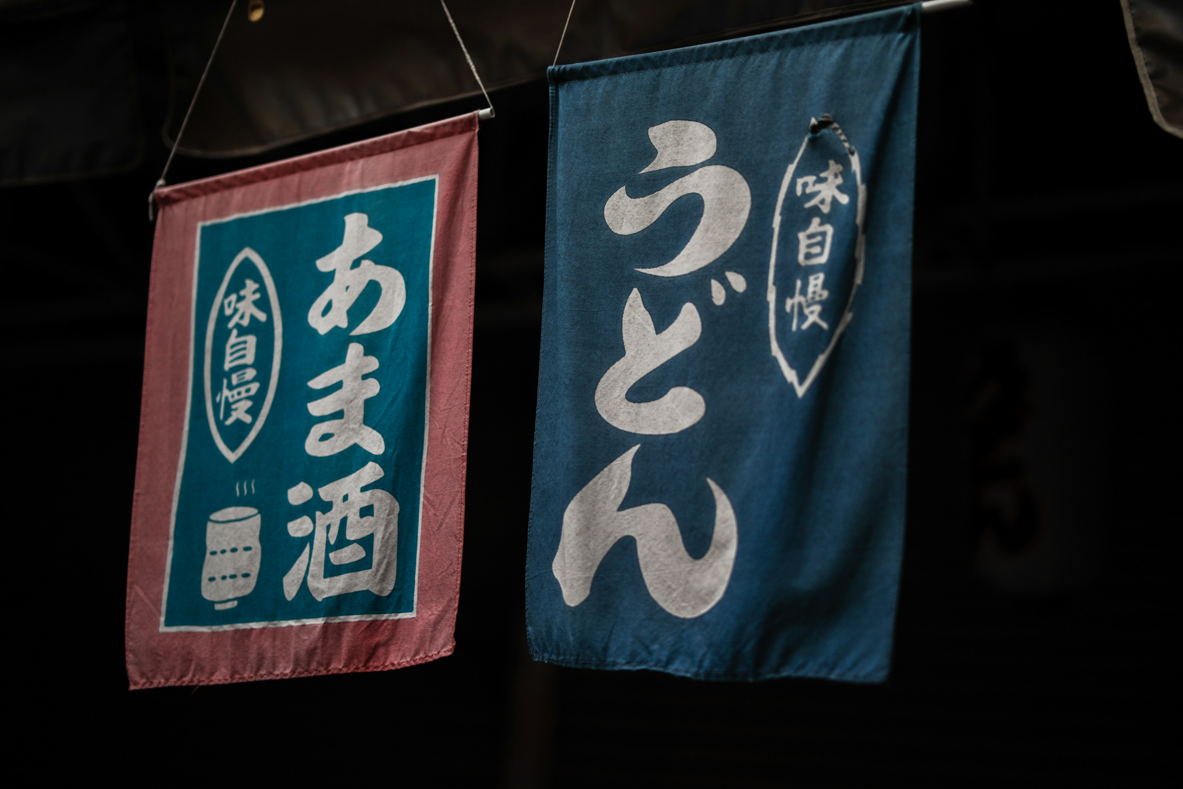 Blue noren with the word 'udon' and pink noren with the word 'amazake' displayed