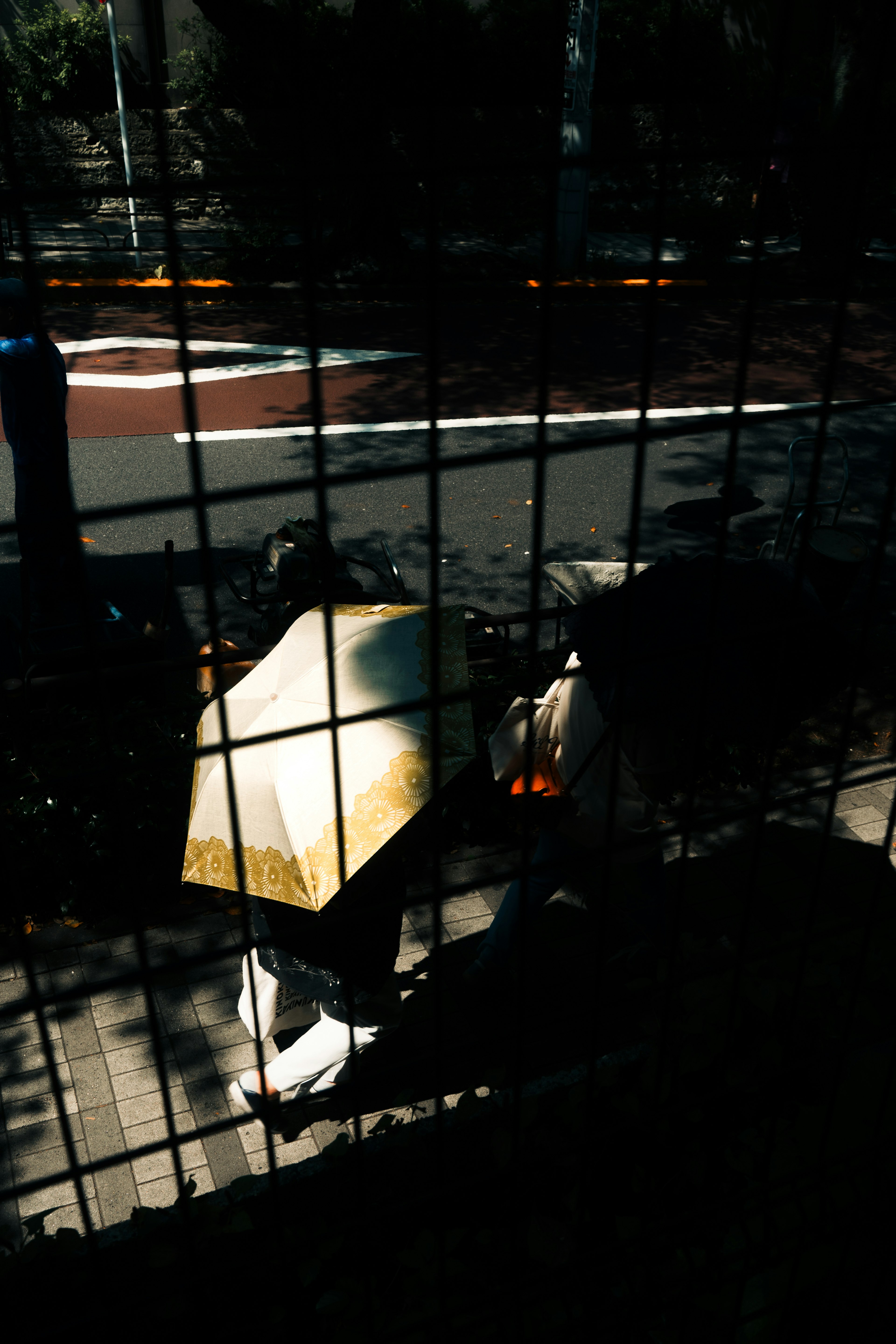 A street scene with a person walking under an umbrella surrounded by a grid fence