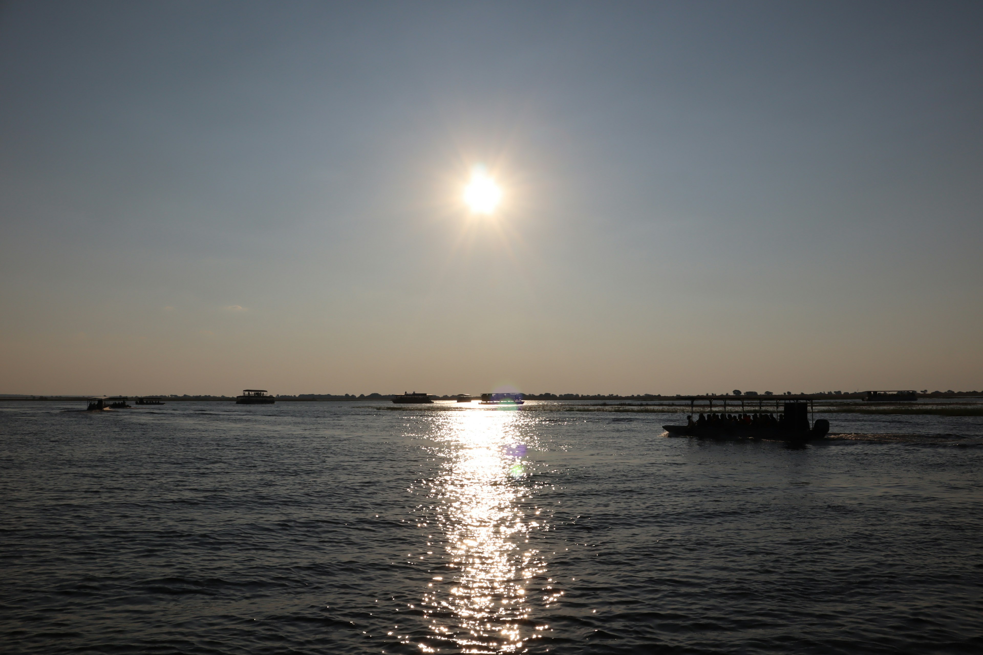 Boats on the water under a bright sun with shimmering reflections