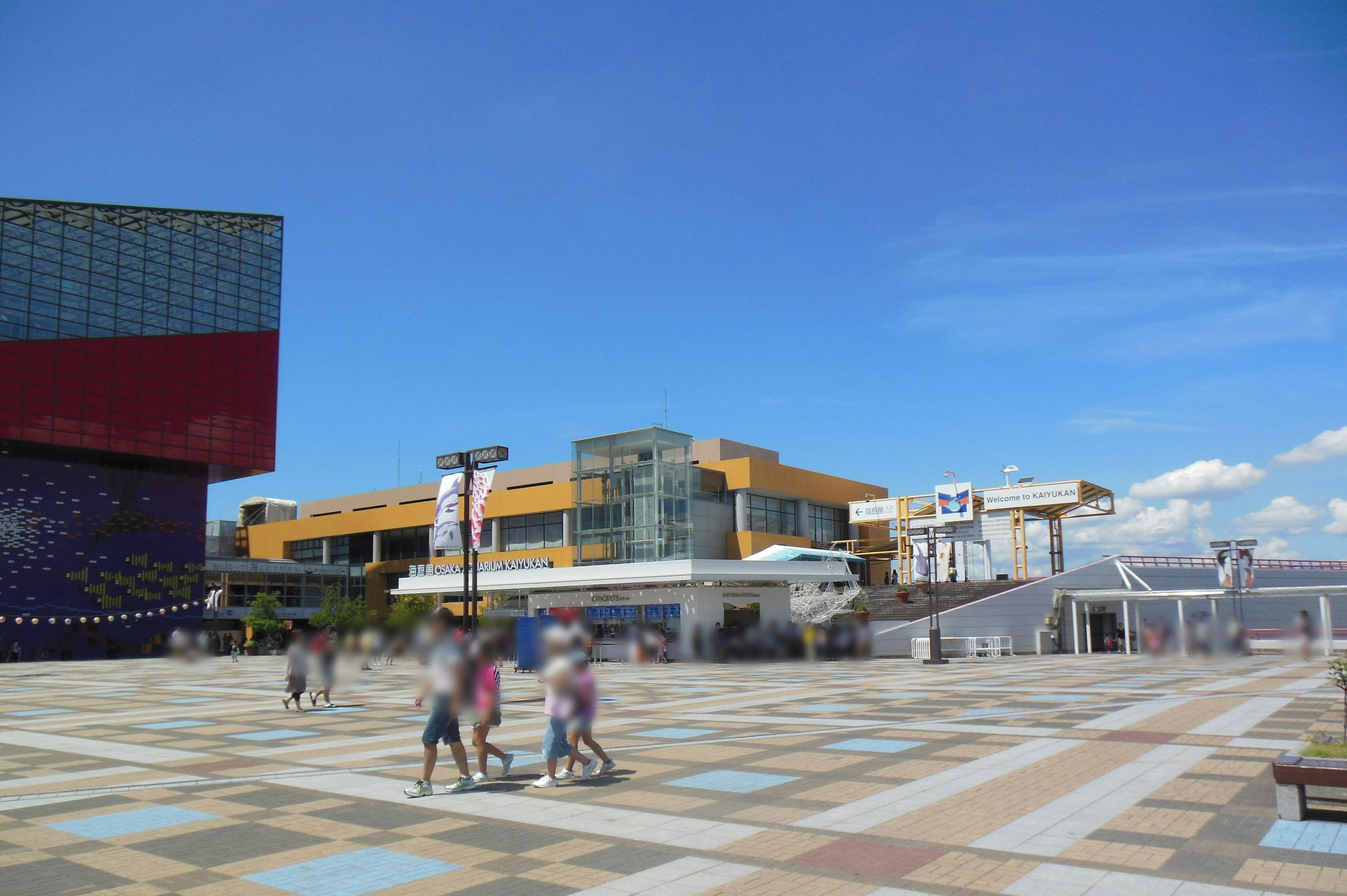 Persone che camminano in una piazza sotto un cielo blu con edifici colorati