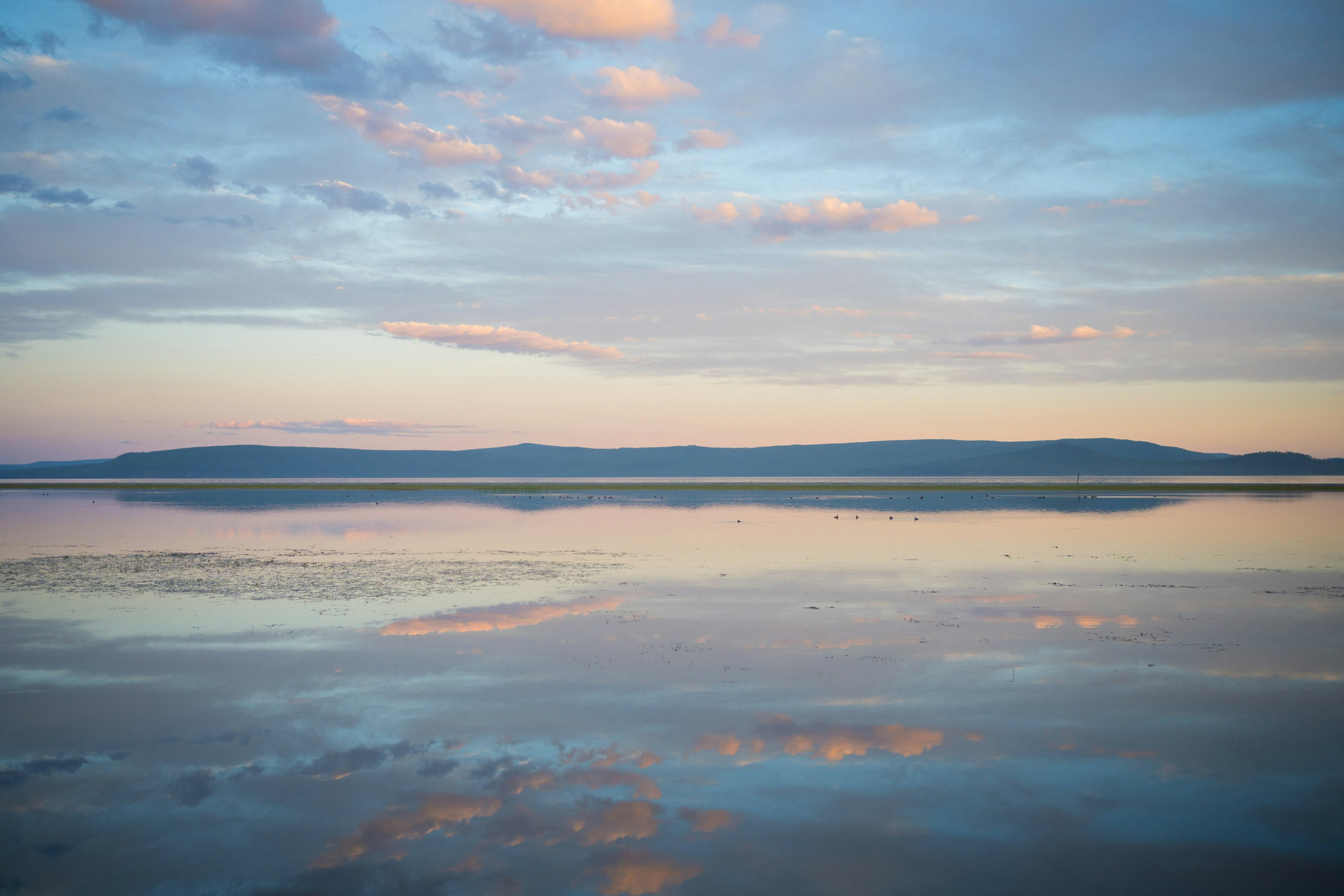 Ruhige Wasseroberfläche, die den Himmel und die Wolken mit schönen blauen und orangefarbenen Farbtönen spiegelt