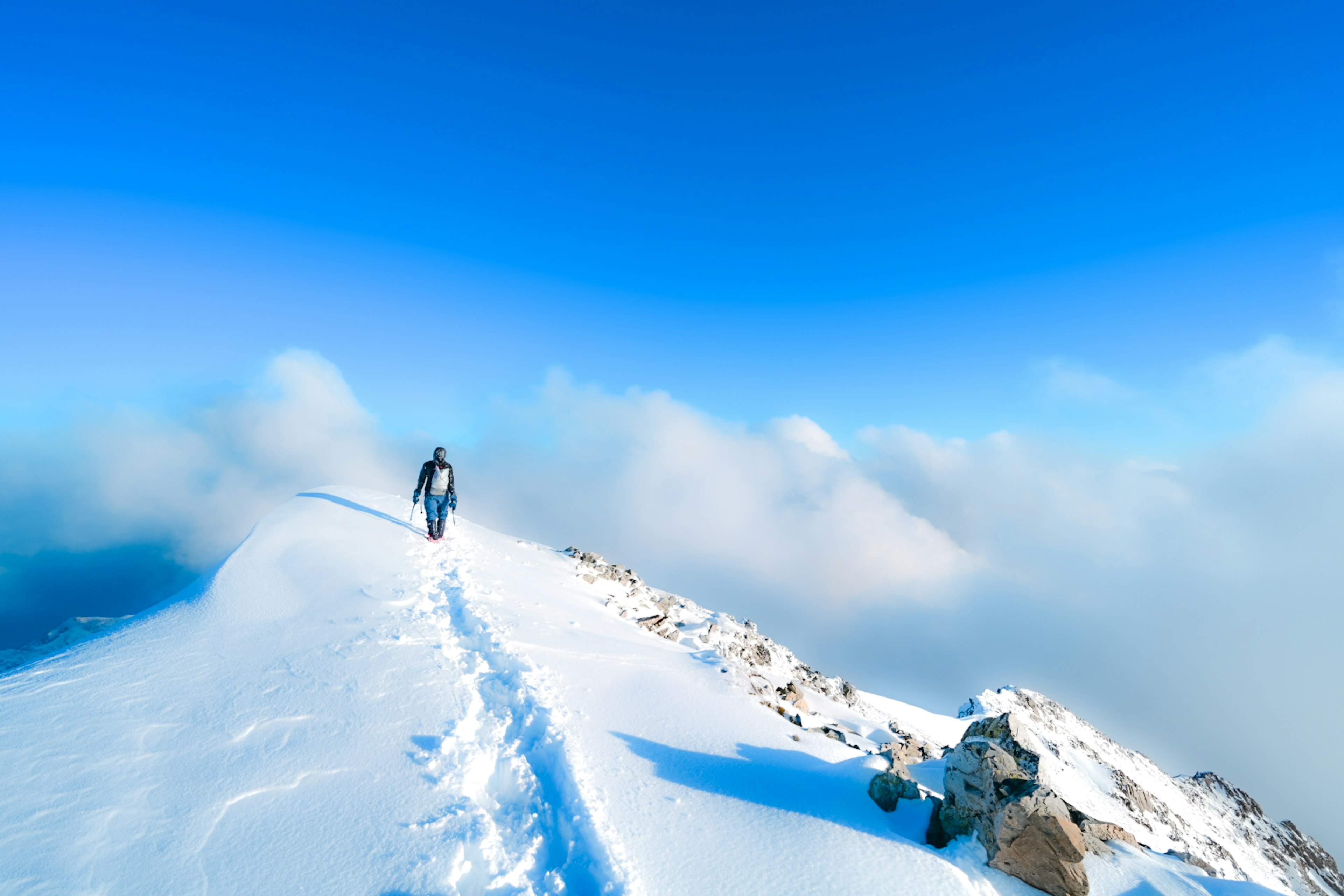 Una persona che cammina su una vetta di montagna coperta di neve sotto un cielo blu