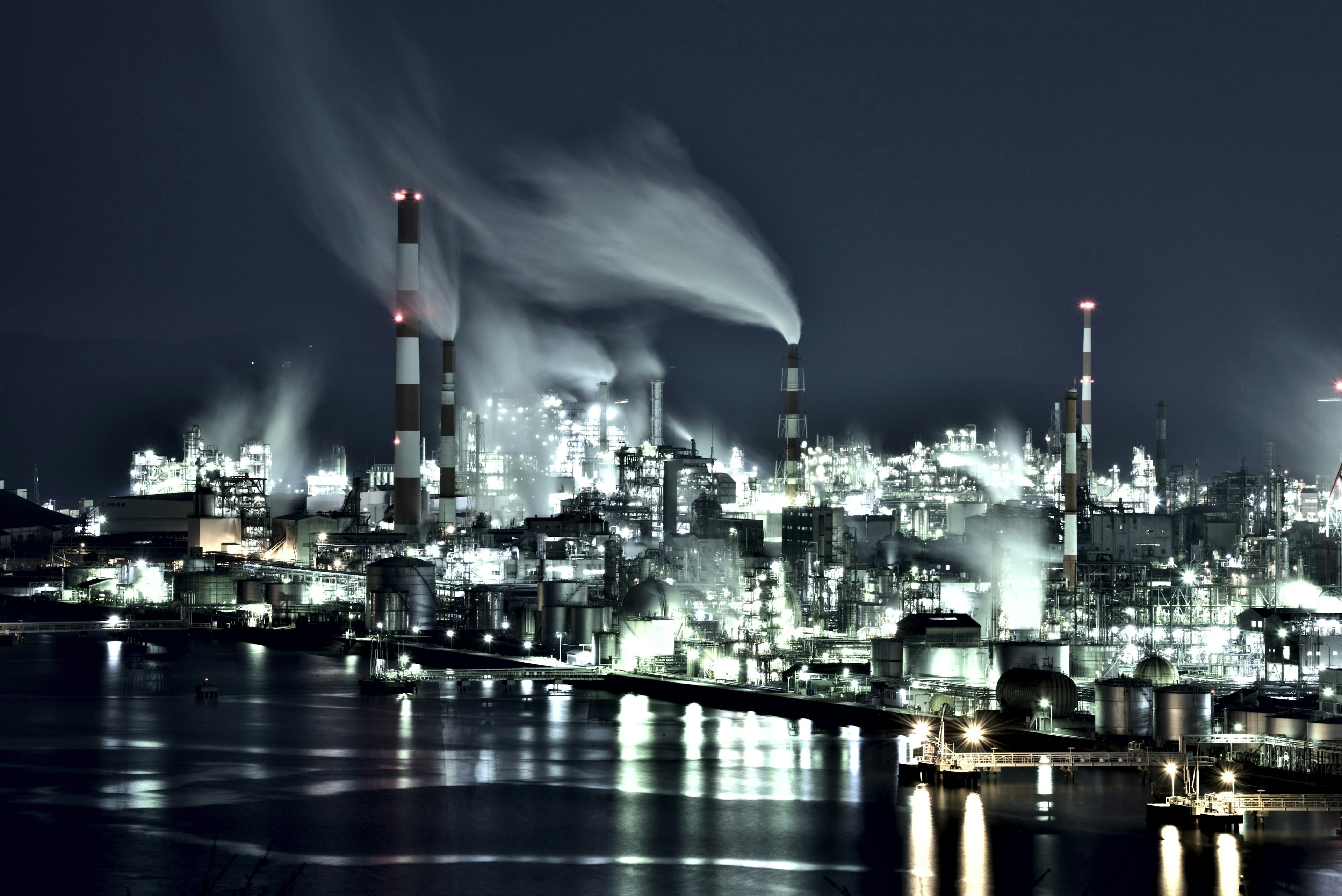 Industrial complex at night with smoke rising from chimneys