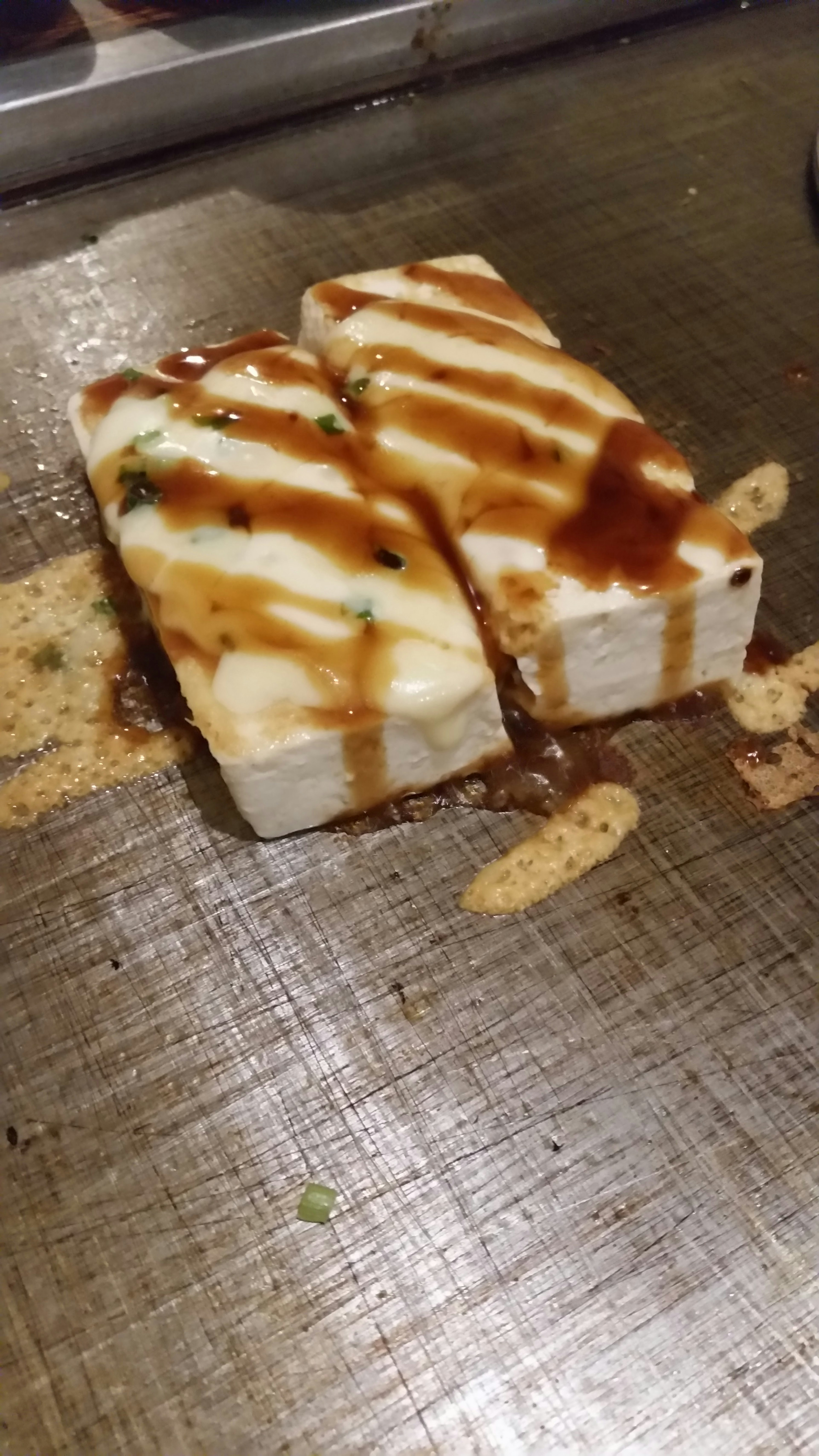 Grilled tofu topped with sauce on a metal surface