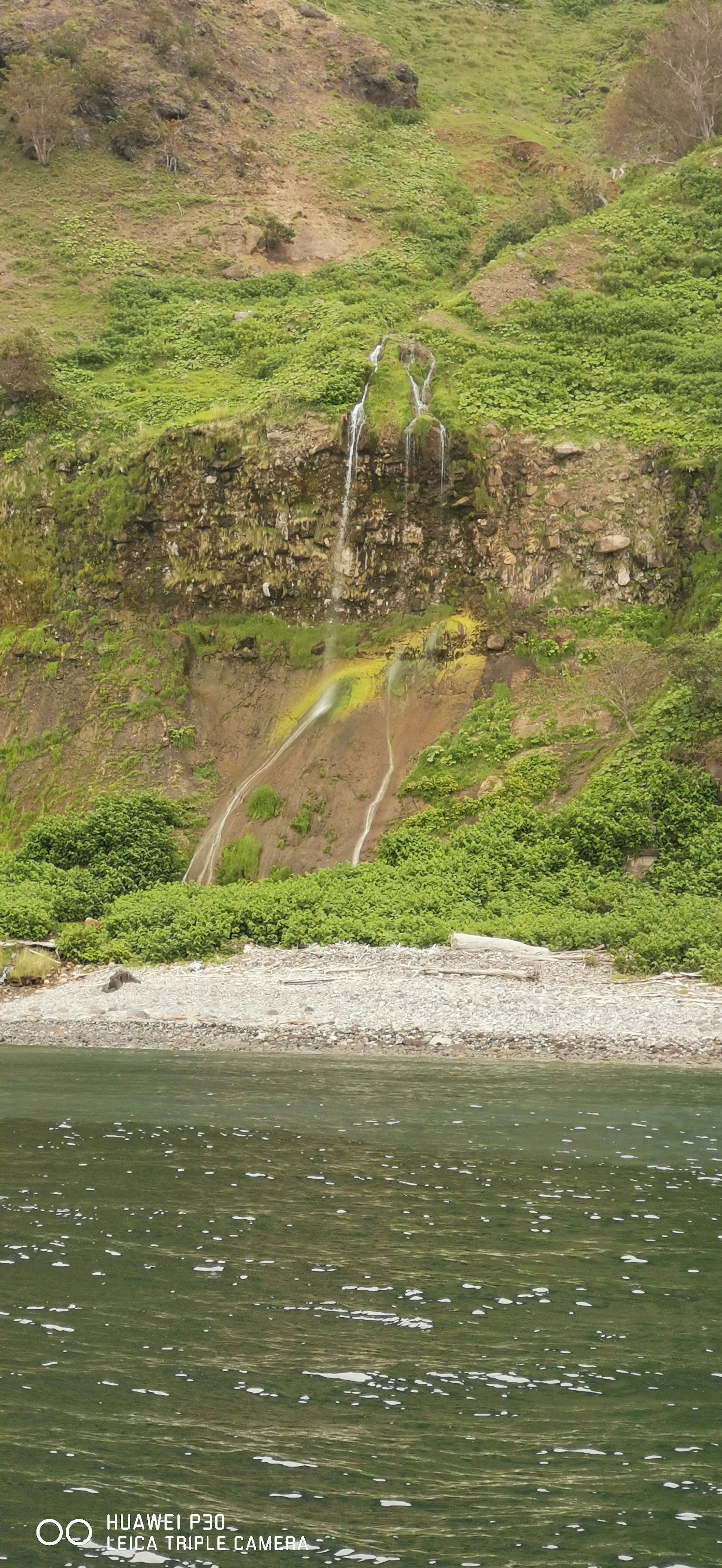 Gambar air terjun kecil yang mengalir dari bukit hijau