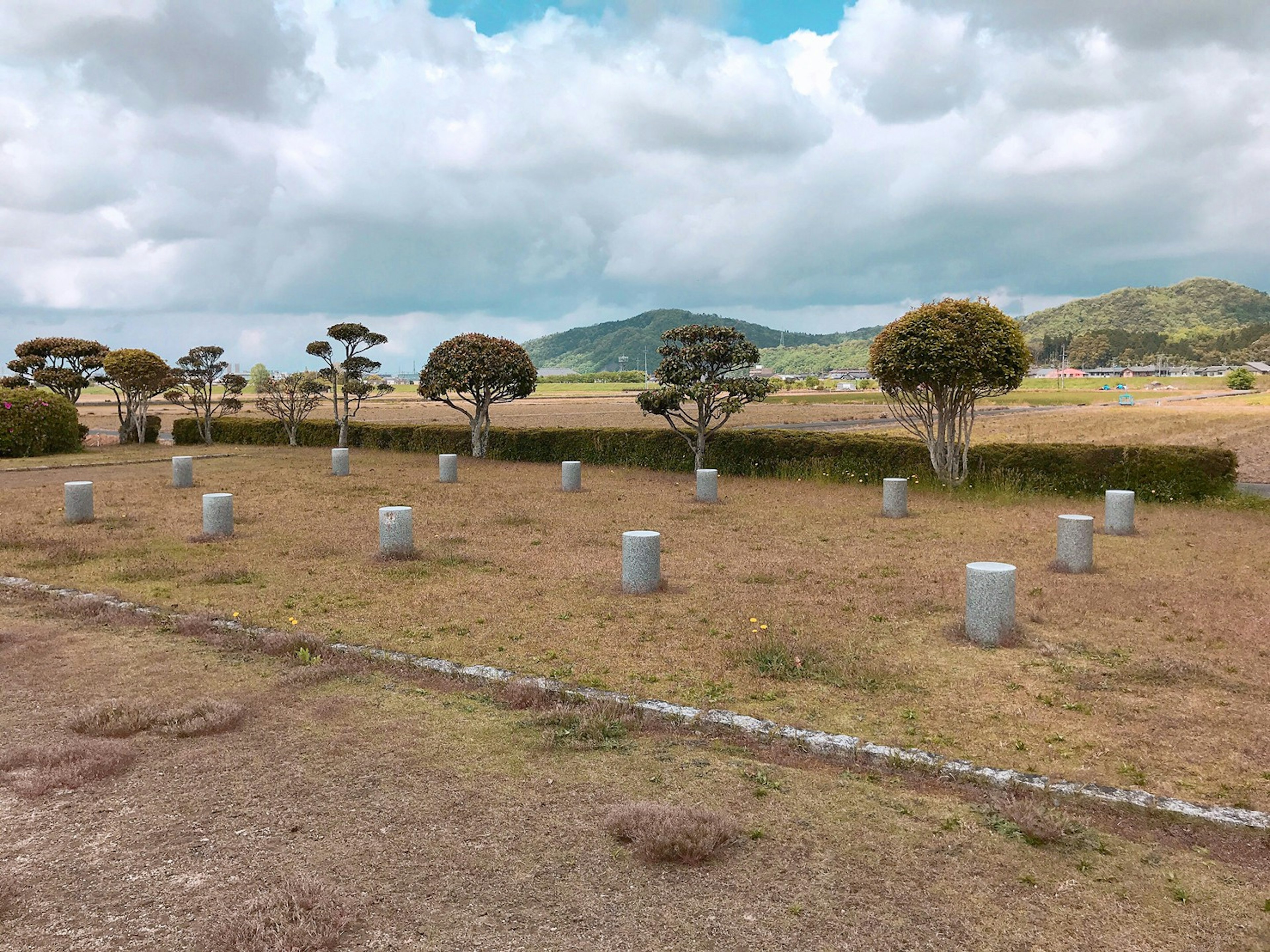 Un large champ herbeux avec des piliers de pierre disposés et des arbres