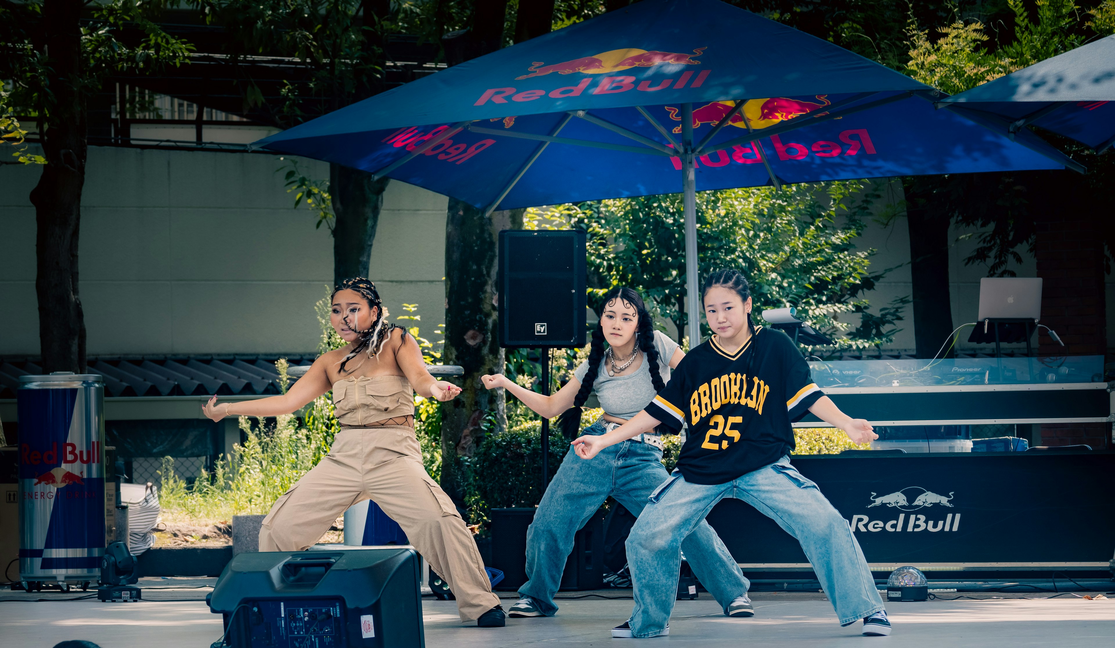 Three dancers performing on an outdoor stage with Red Bull umbrellas in the background