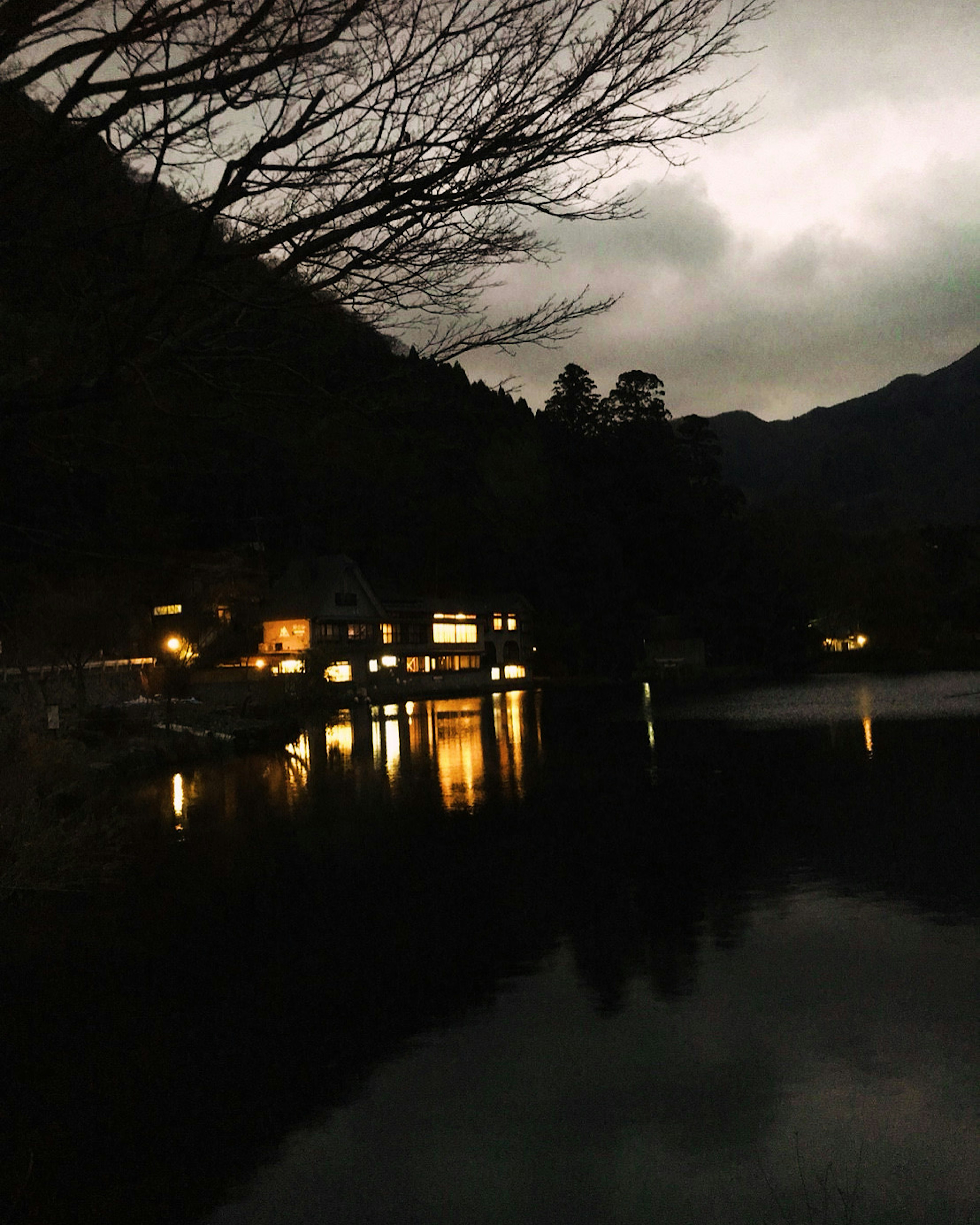 Lago nocturno tranquilo reflejando luces y silueta de montañas