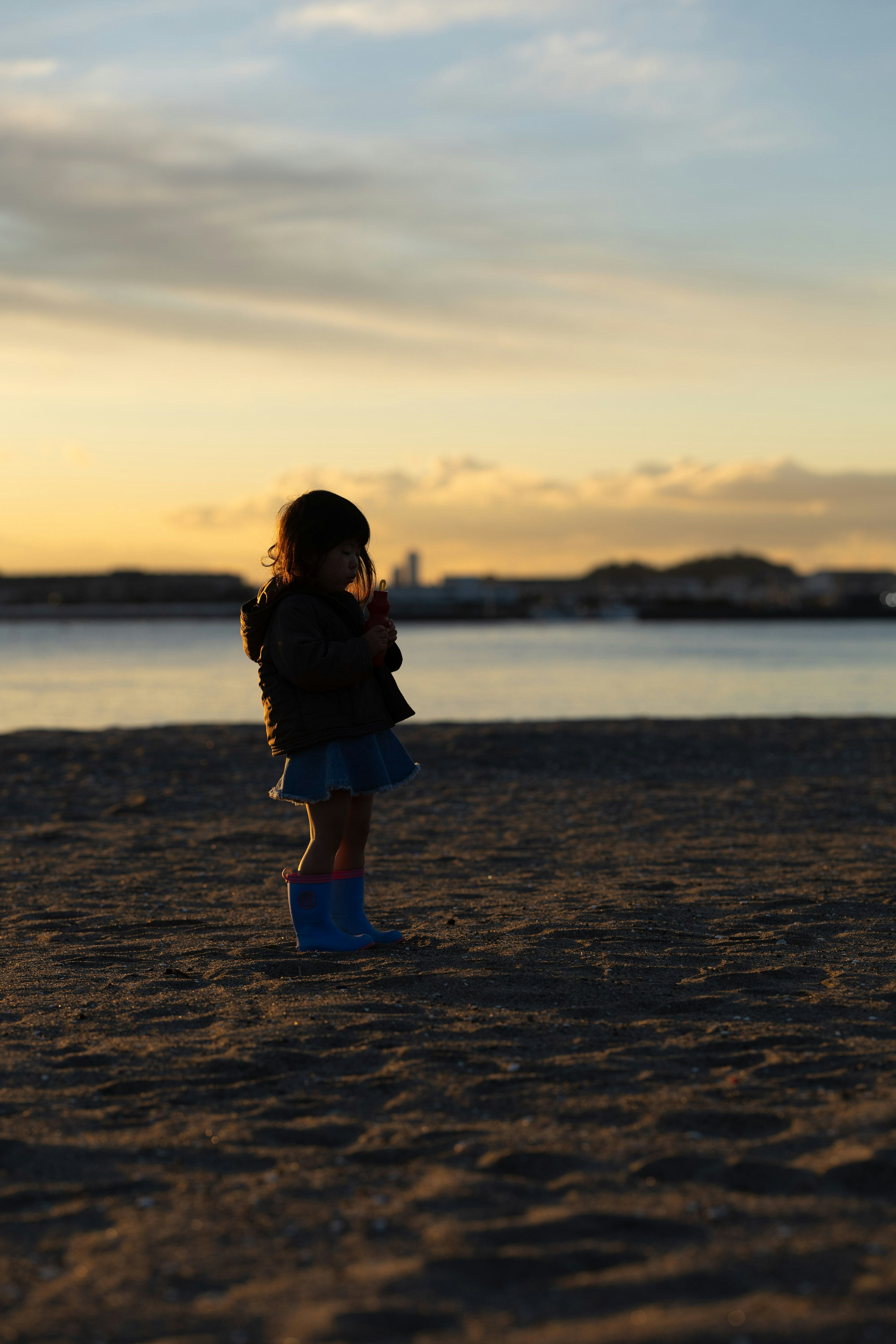 夕日を背にした子供が砂浜に立っている
