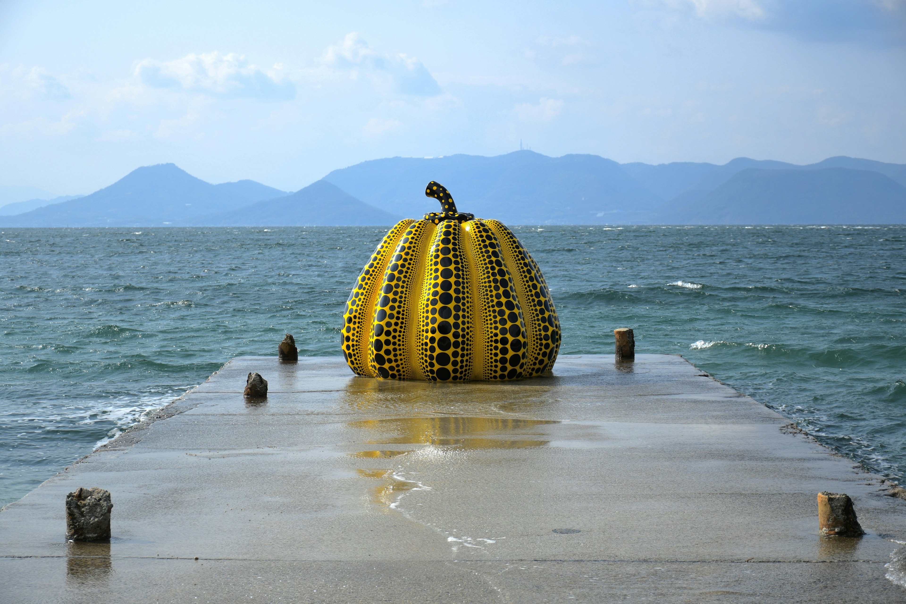 Una escultura de calabaza amarilla en un muelle con vista al mar y las montañas