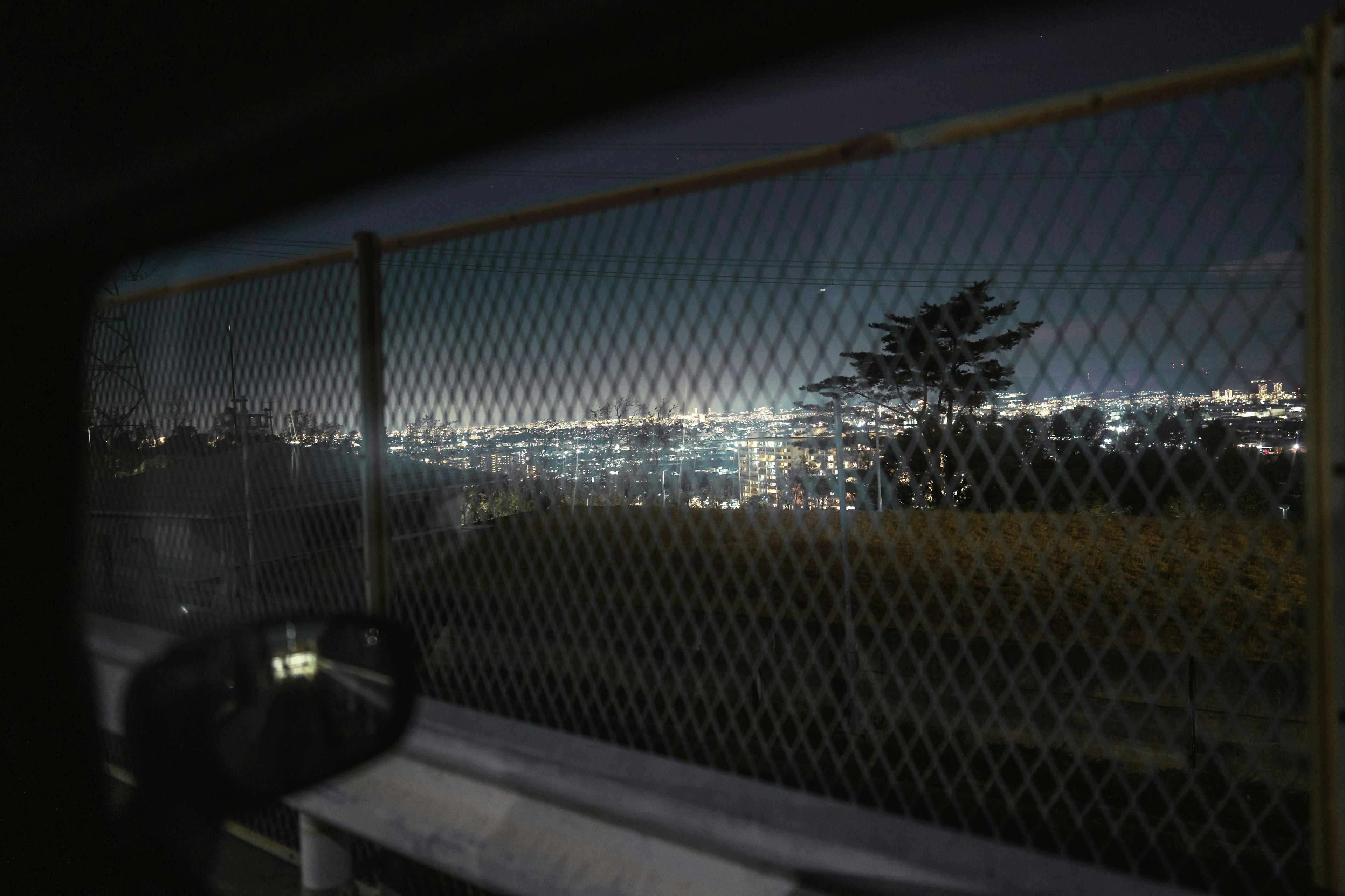 Night view of a city skyline through a fence