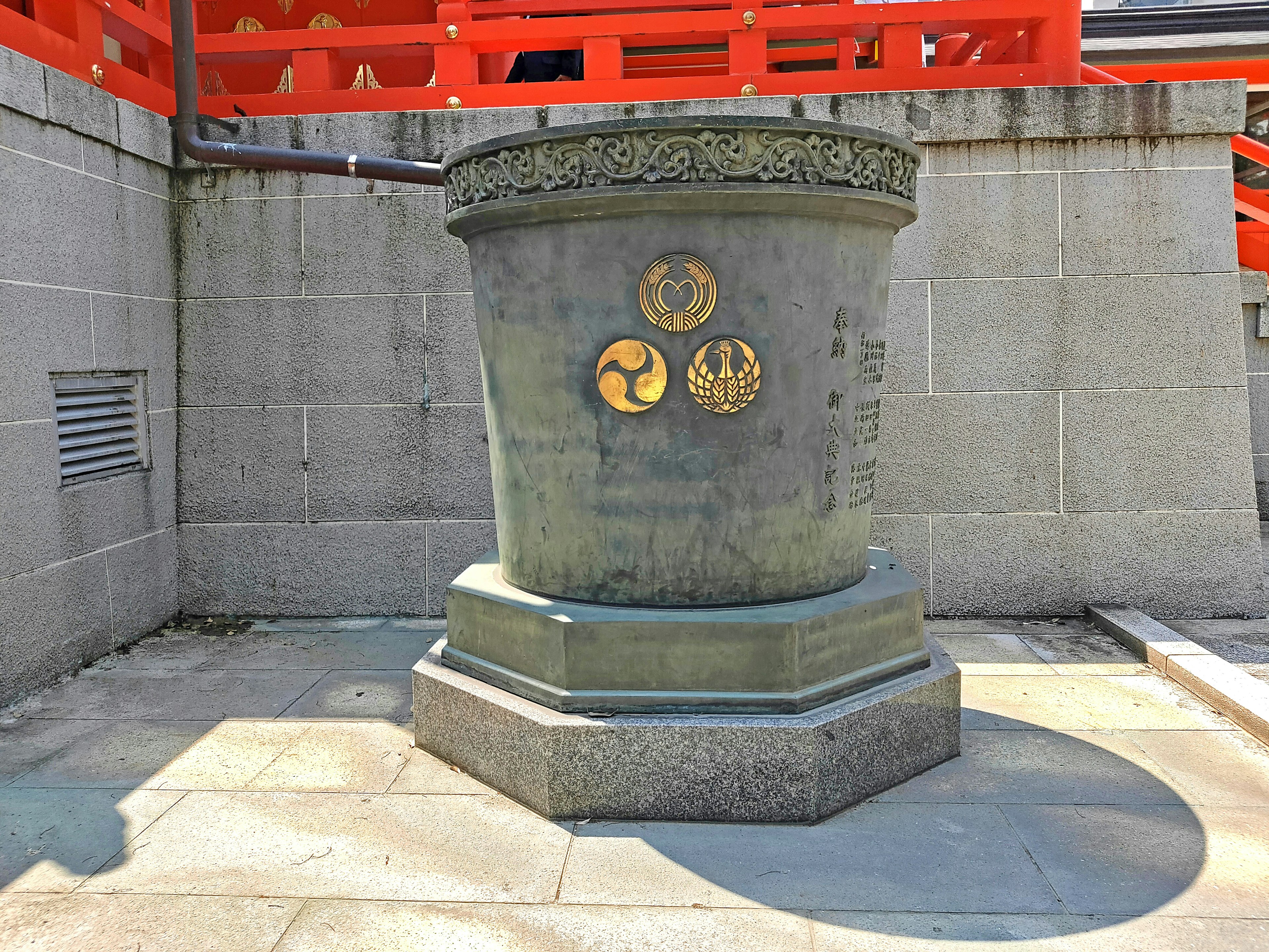 Dekorativer Steinpfeiler in der Nähe eines roten Torii mit drei goldenen Emblemen