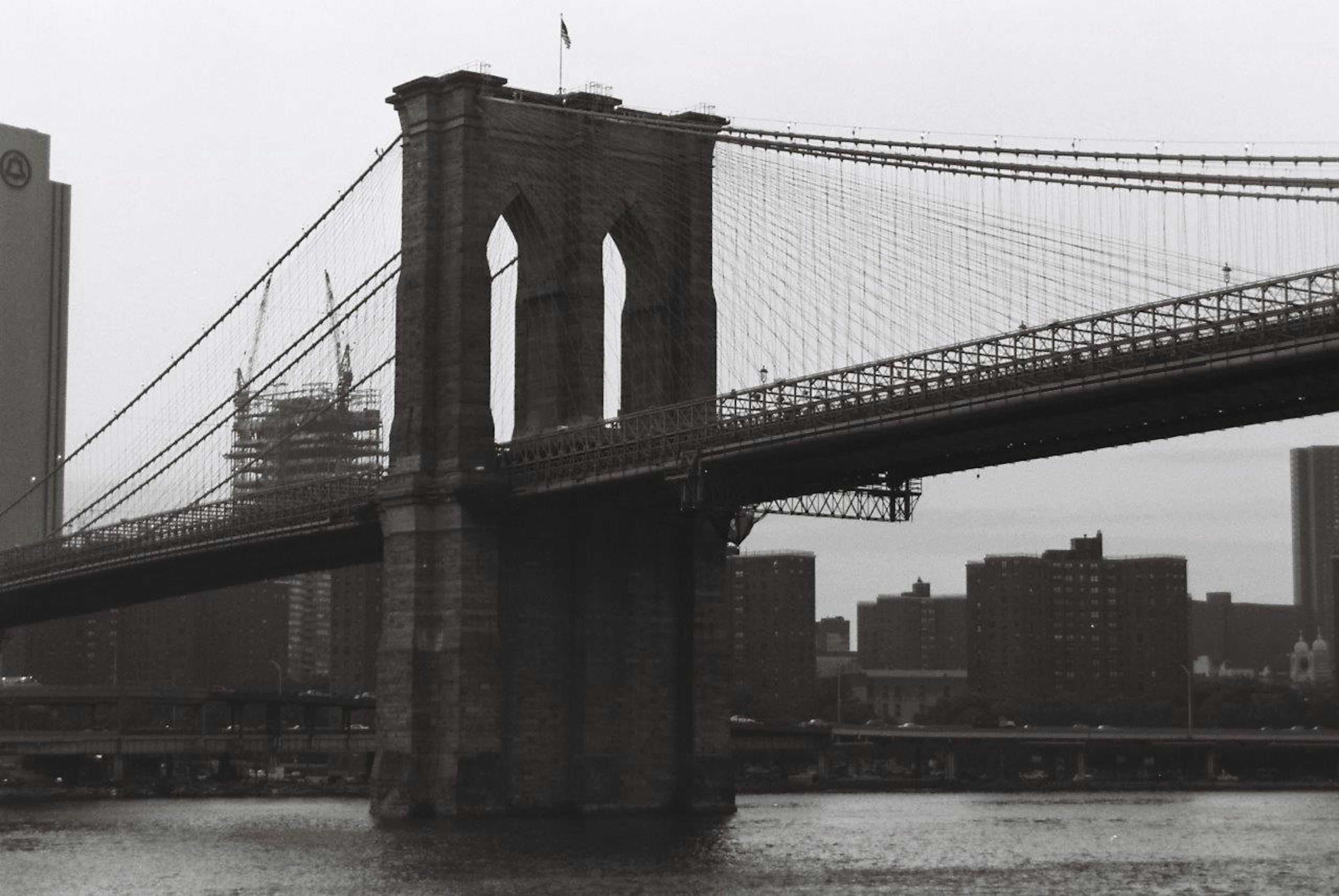 Gambar hitam putih Jembatan Brooklyn dengan gedung di sekitarnya