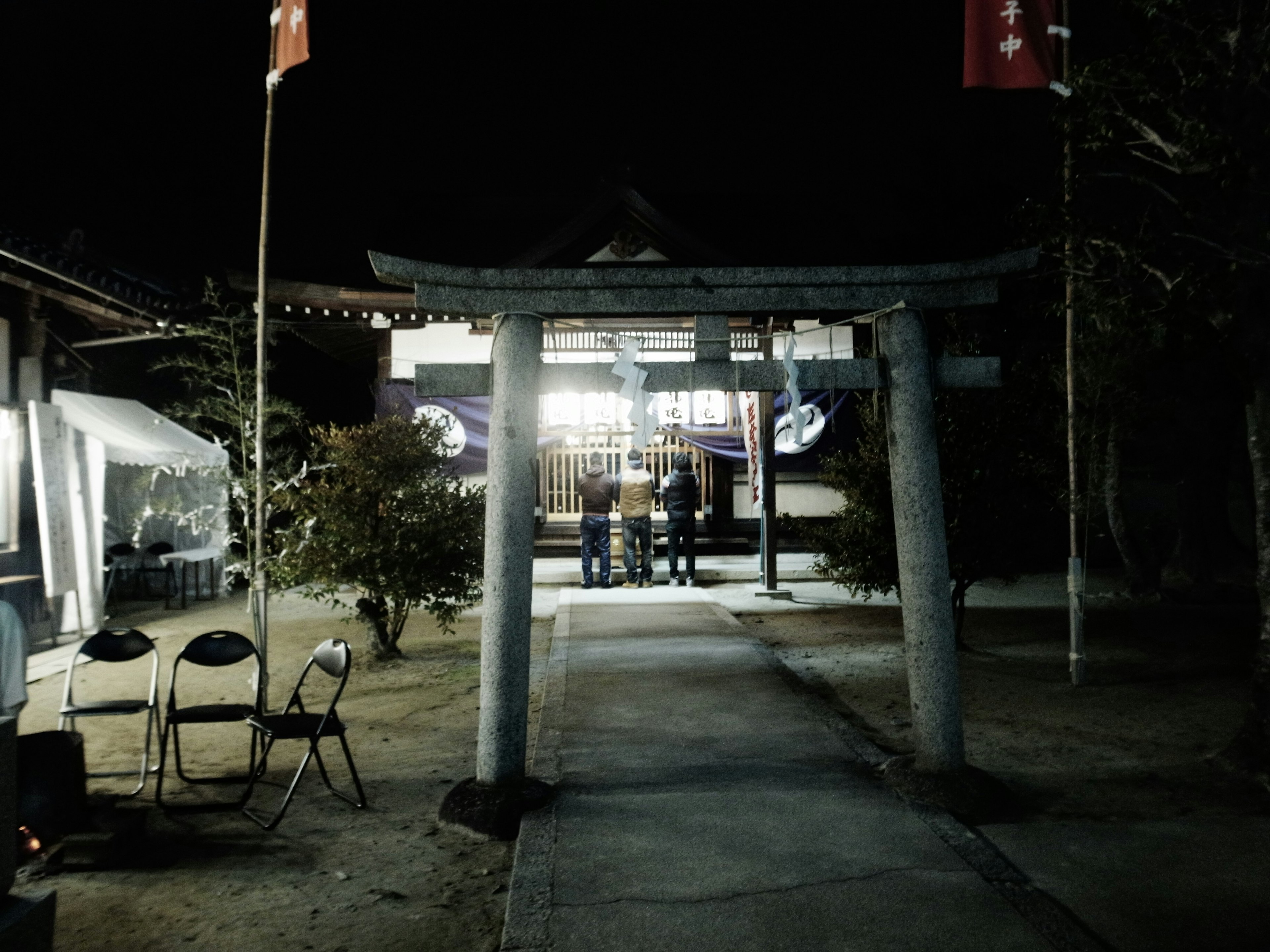 Puerta torii de noche con personas frente a un santuario