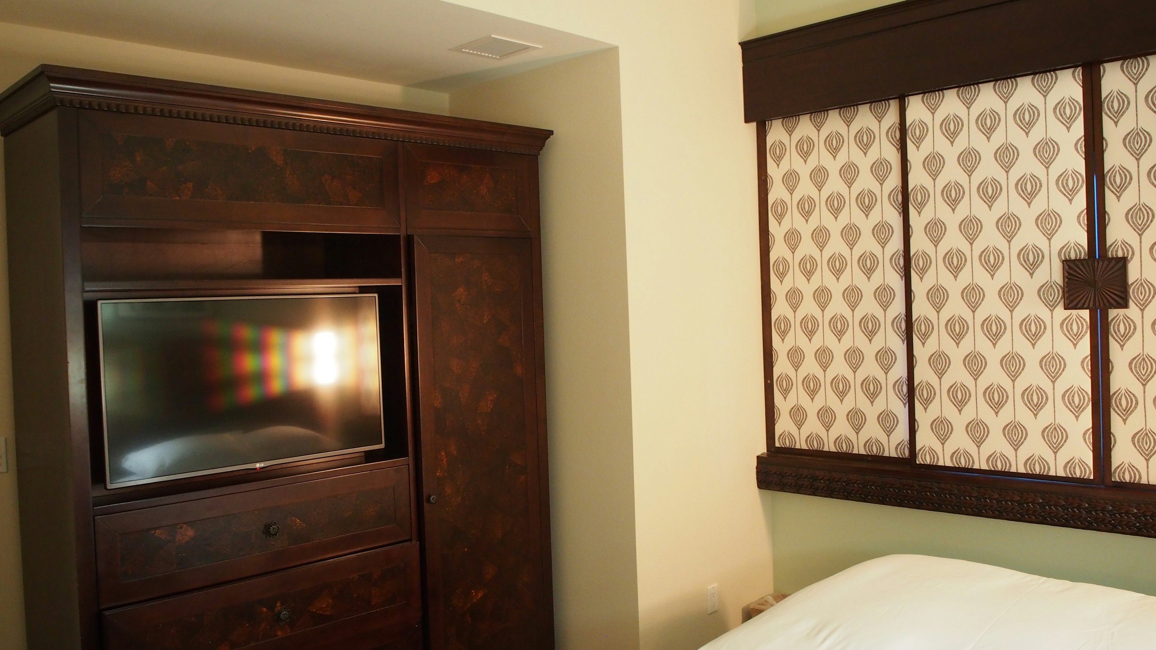 A bedroom featuring a dark wooden cabinet with a television and decorative curtains at the window