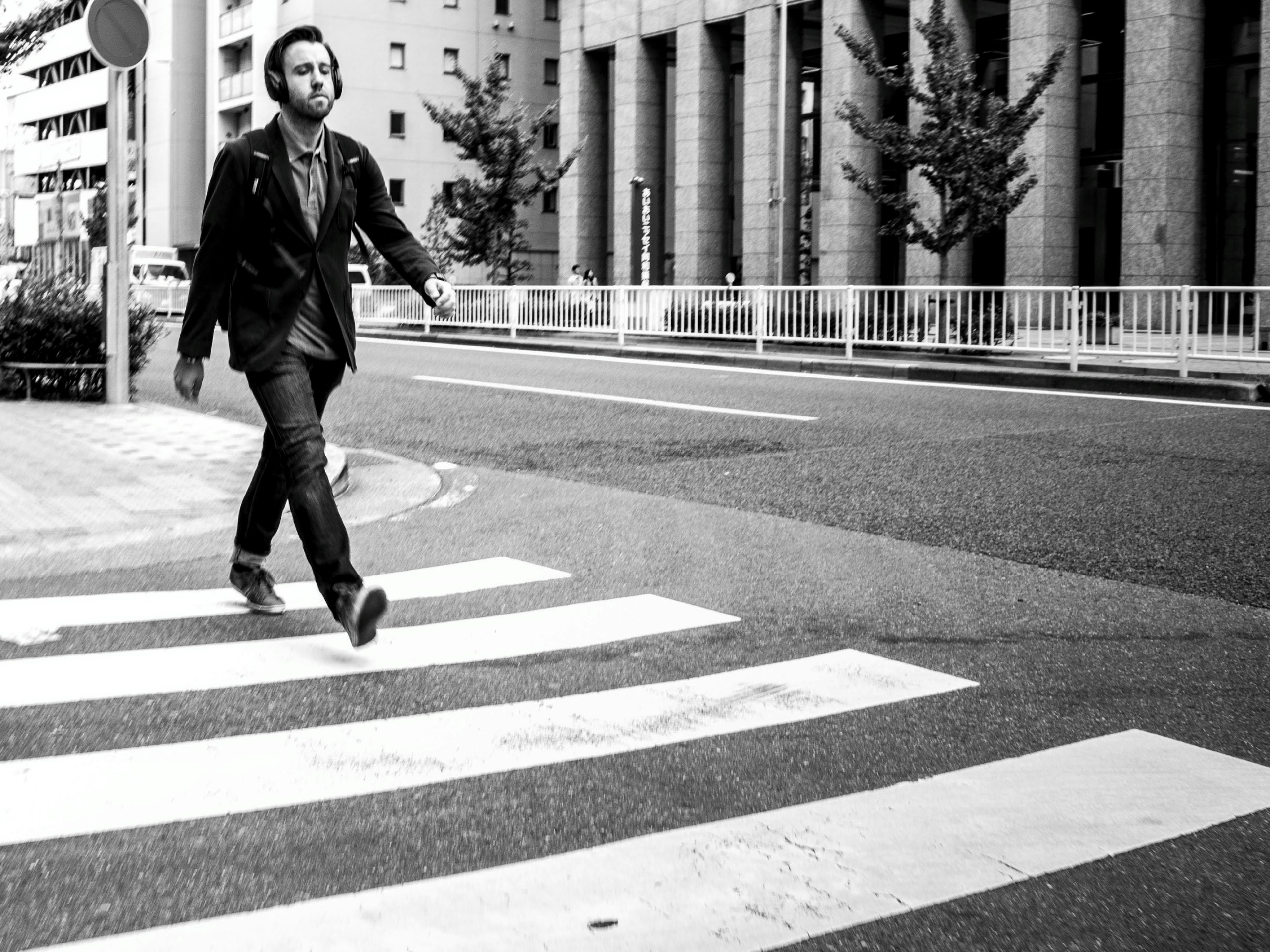 A man walking across a crosswalk in a black and white photo with buildings in the background