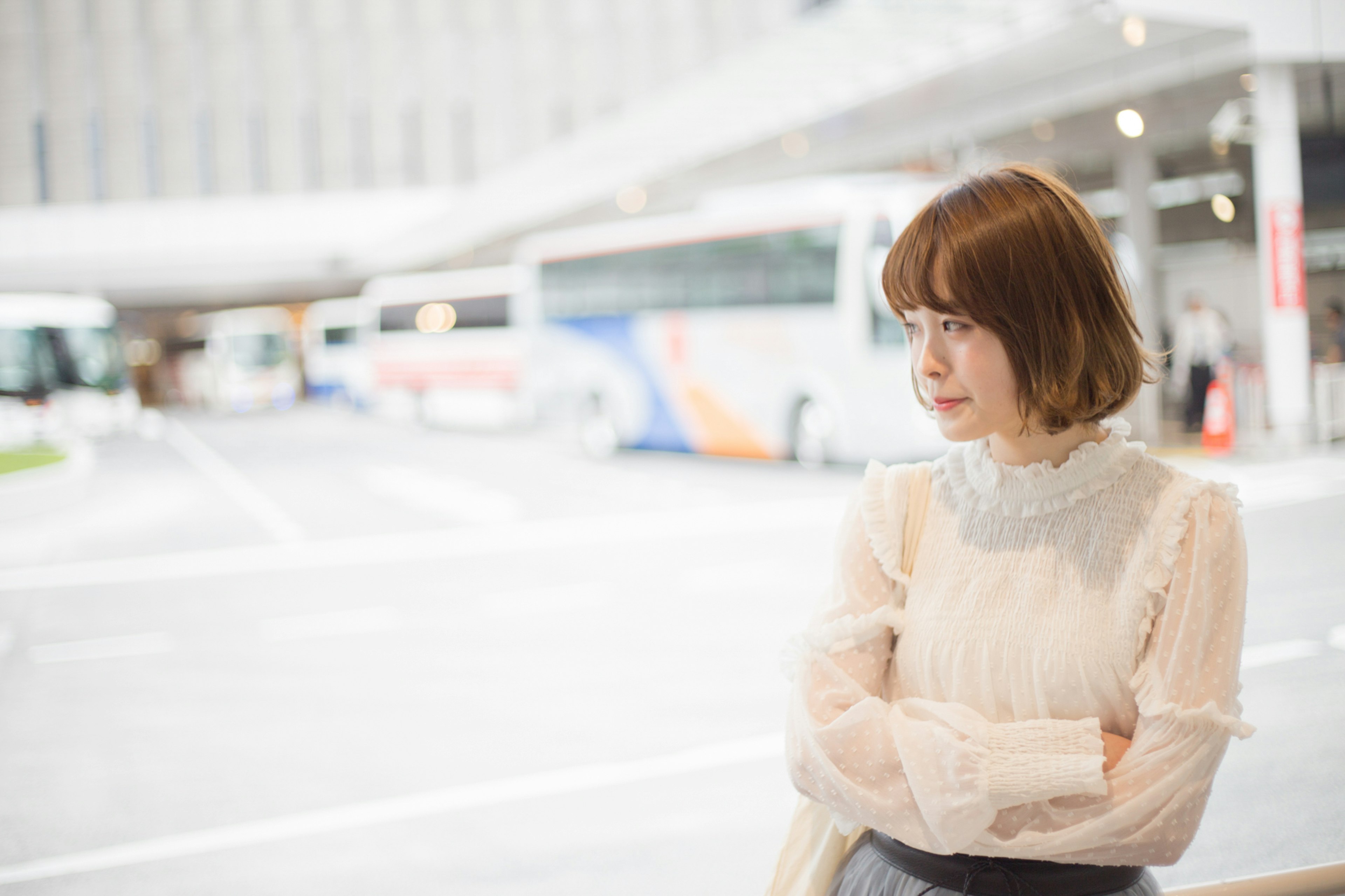 Portrait d'une femme pensive à un arrêt de bus avec des bus et un bâtiment moderne en arrière-plan