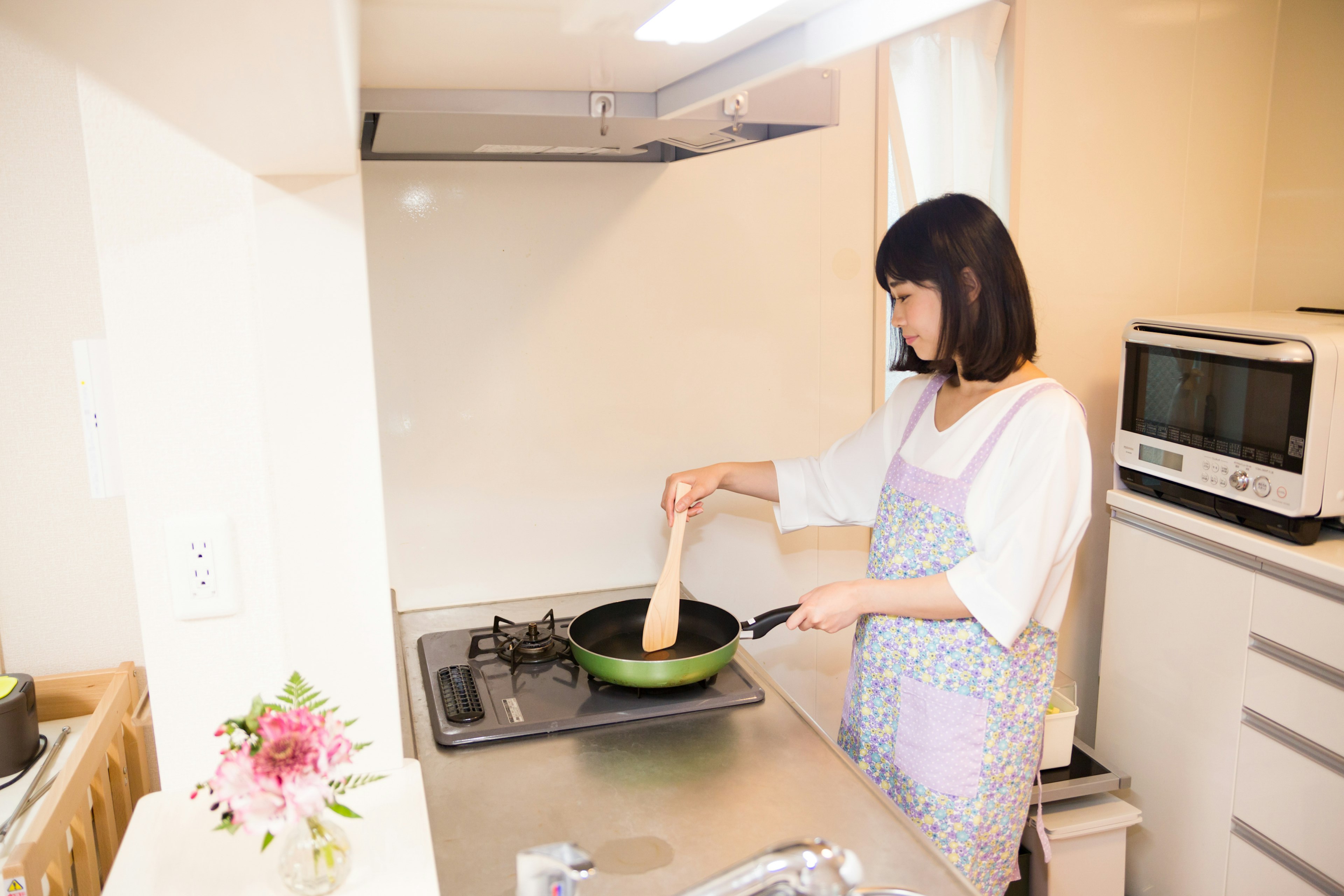 A woman cooking in a kitchen using a frying pan