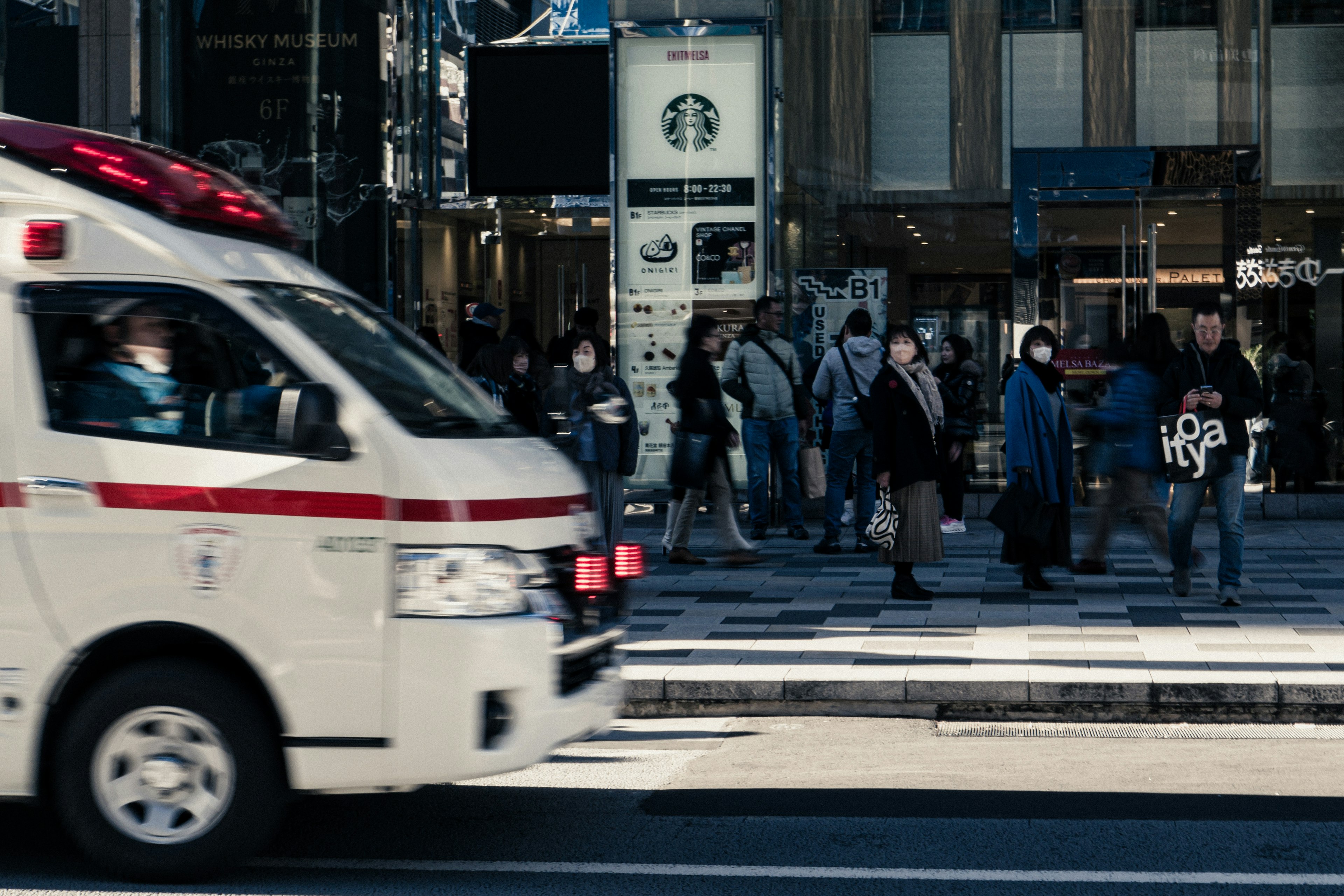 救急車が通り過ぎる繁華街の風景と人々が歩いている様子