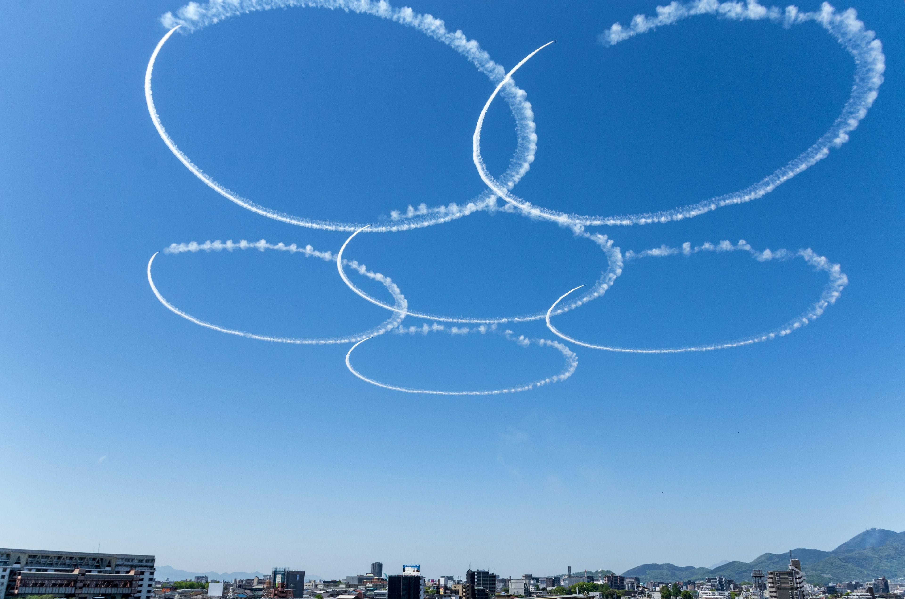 Anelli di fumo bianco contro un cielo azzurro con uno skyline urbano sottostante