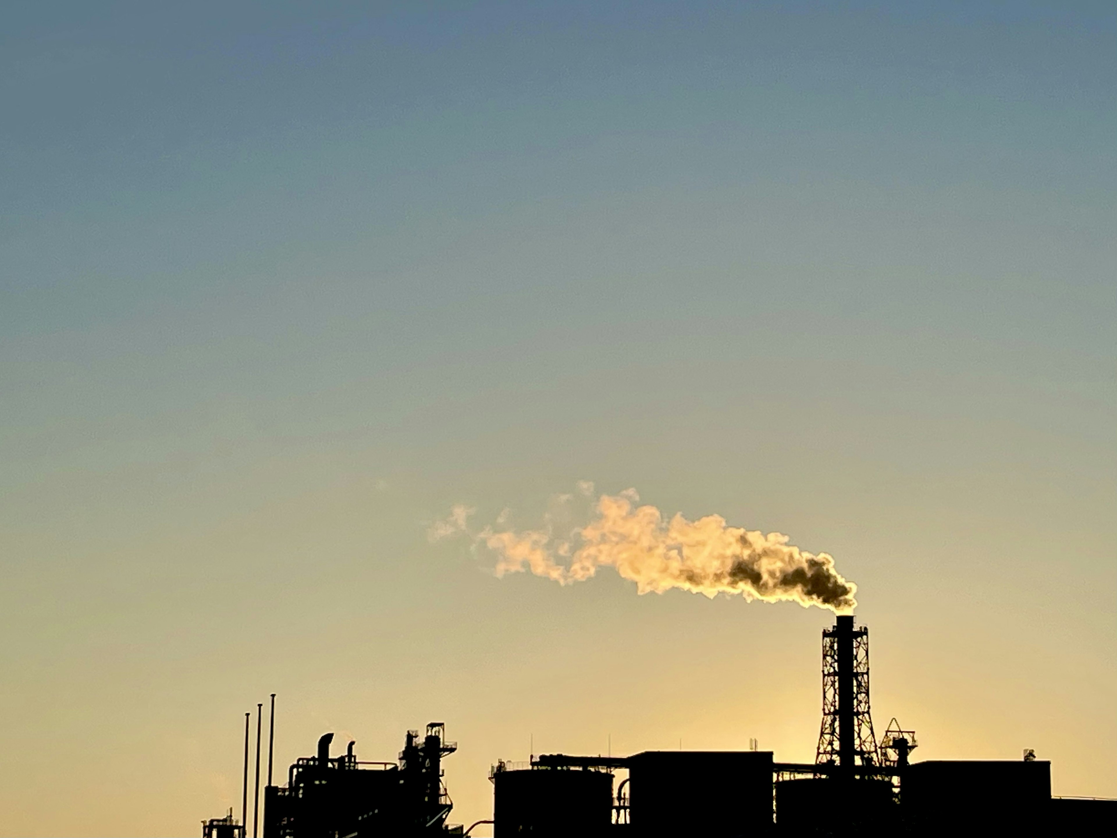 Silhouette of a factory emitting smoke against a sunset sky