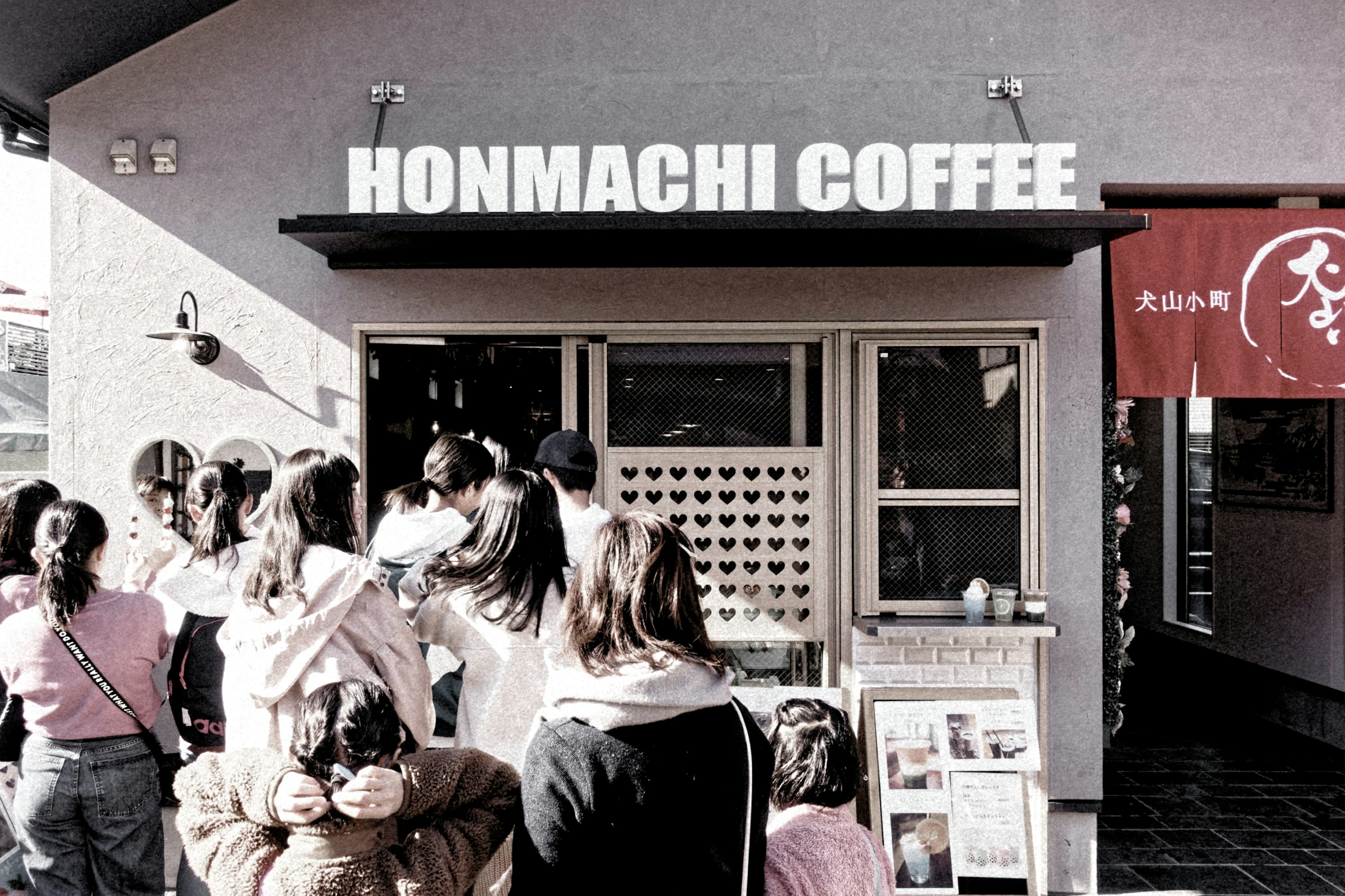 ผู้คนยืนต่อแถวหน้าคาเฟ่ HONMACHI COFFEE พร้อมป้ายที่ชัดเจน