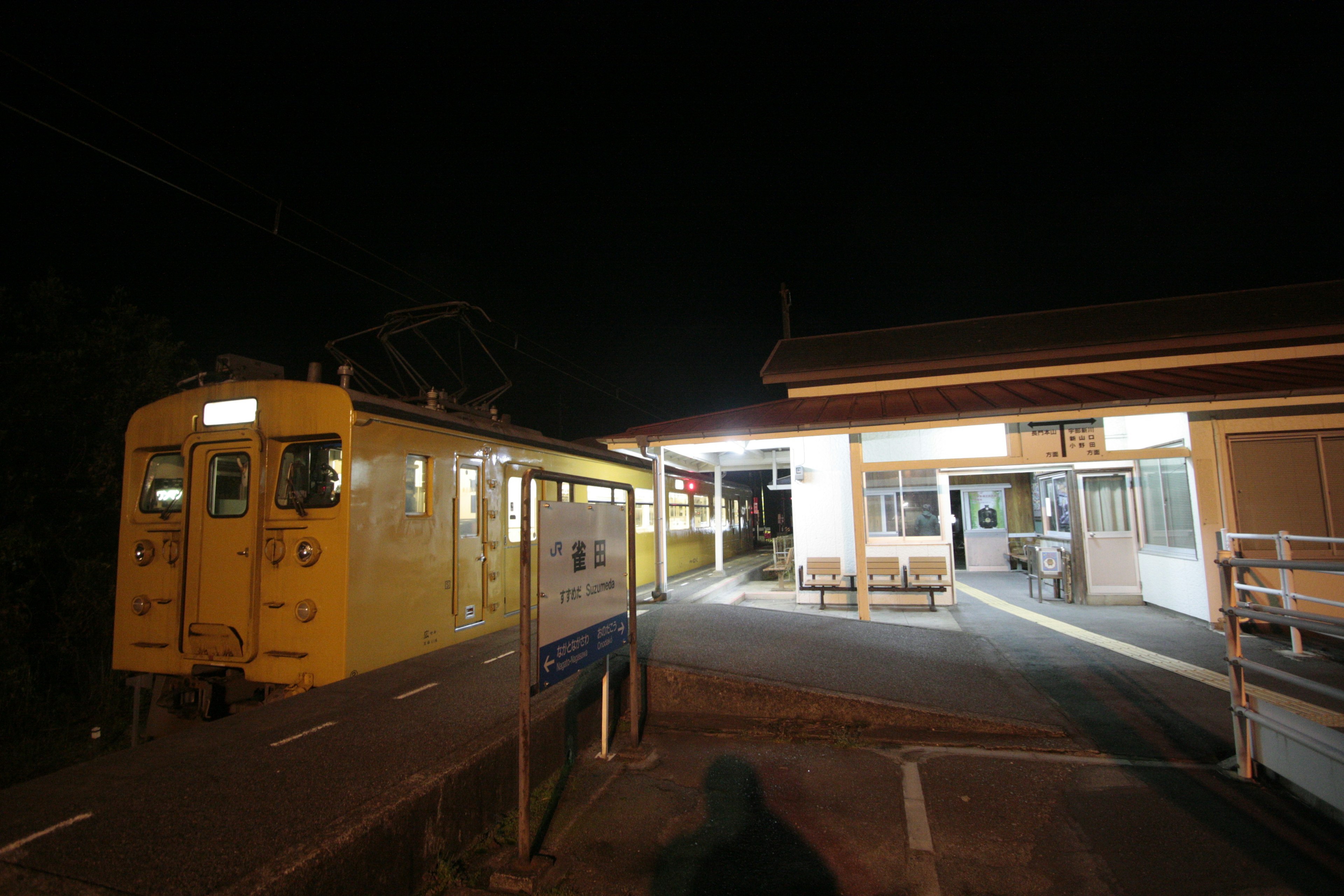 Yellow train at a rural station during the night with surrounding buildings