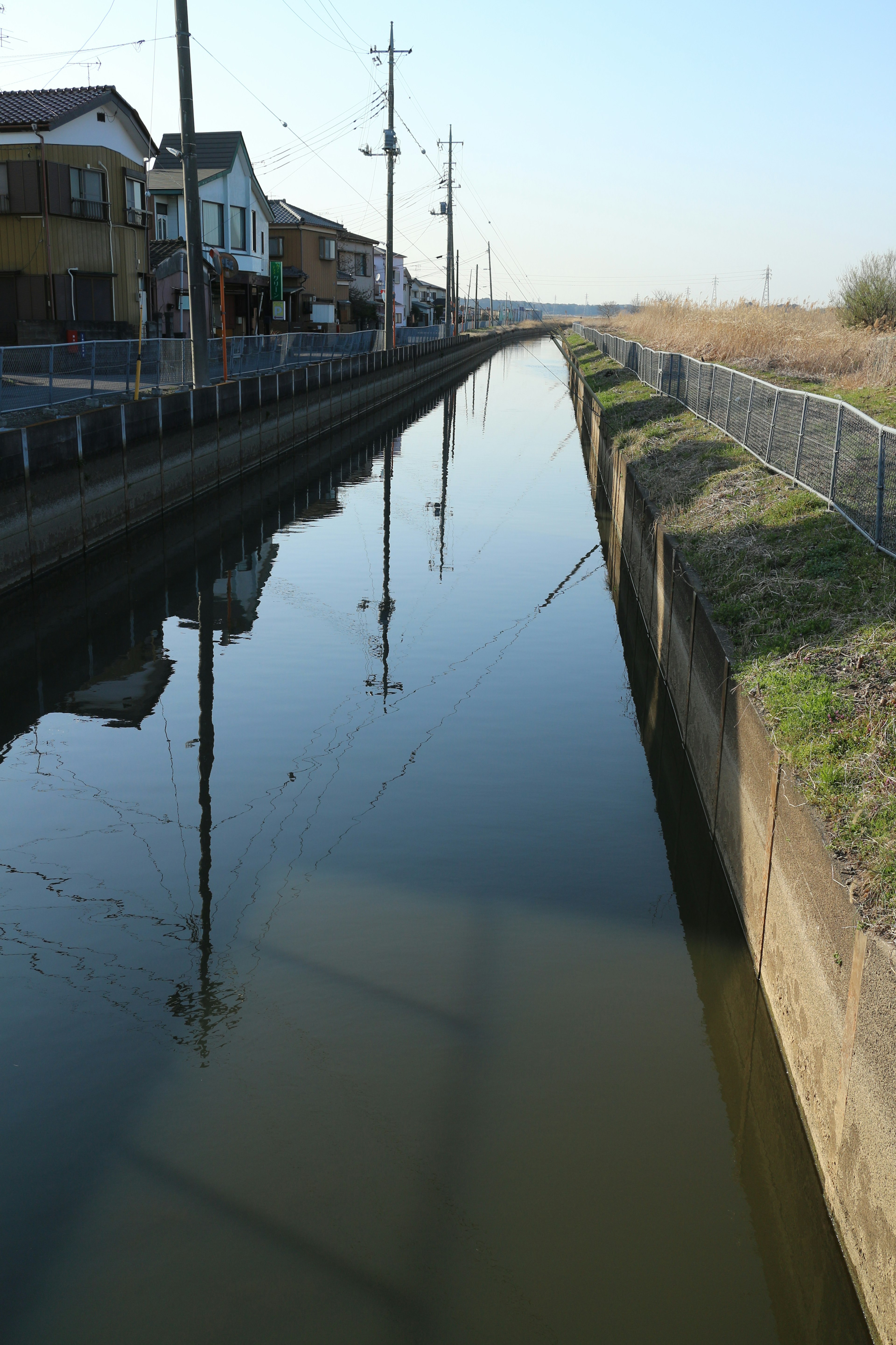 A tranquil waterway reflecting houses and power poles on either side