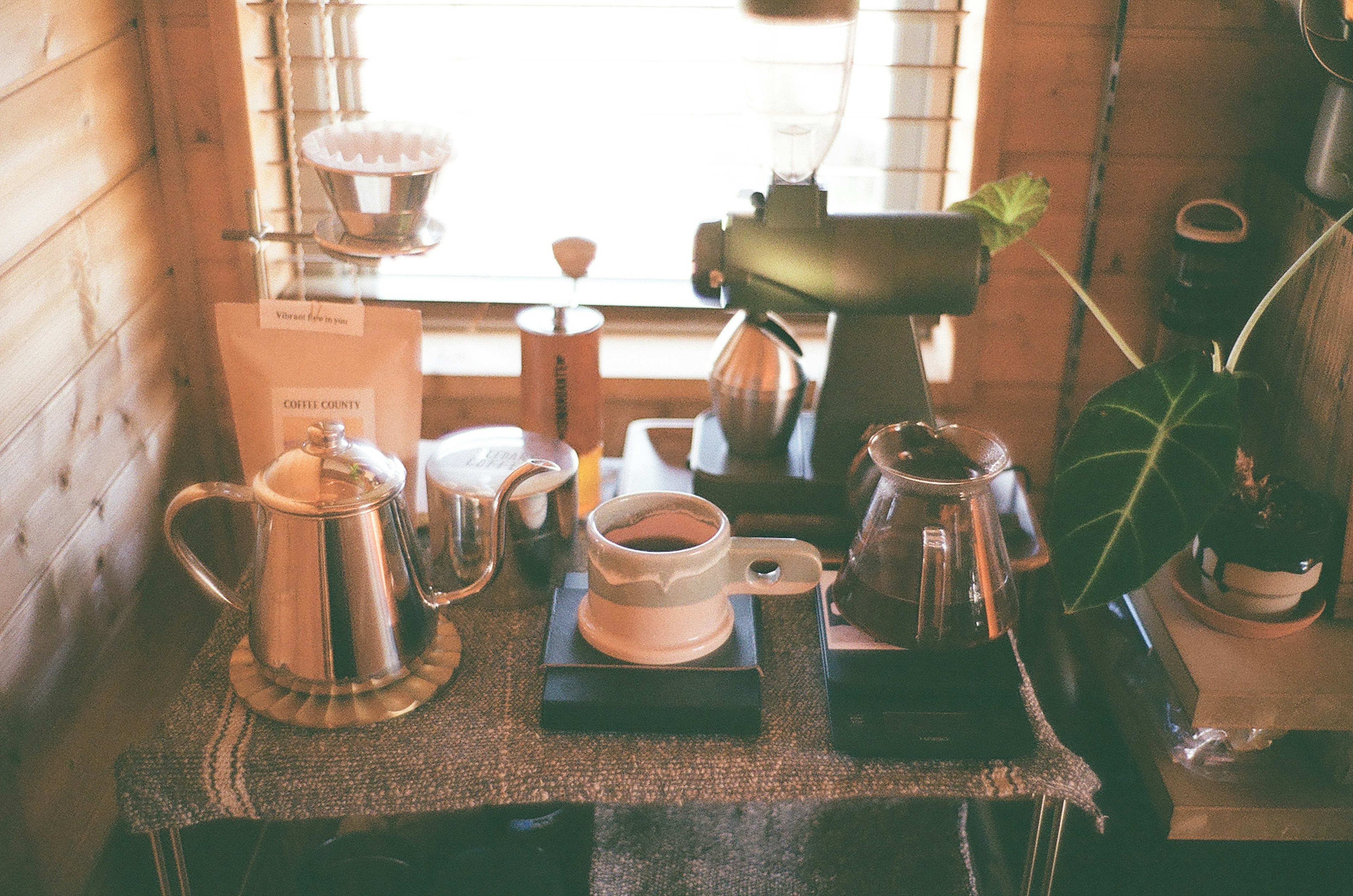 Escena de café acogedora con equipo de café y una planta en una mesa de madera