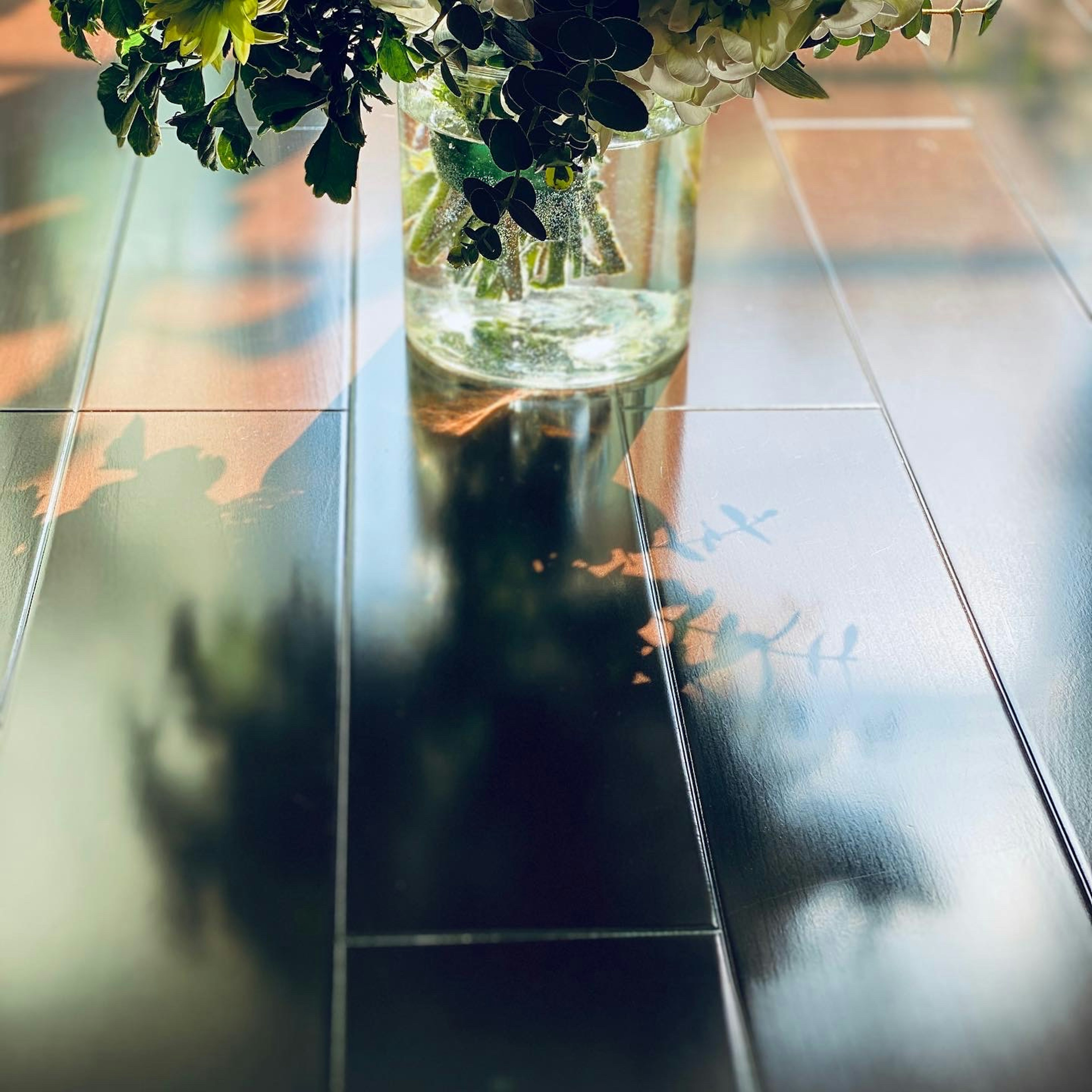 Un vase transparent rempli de plantes vertes et de fleurs posé sur une table