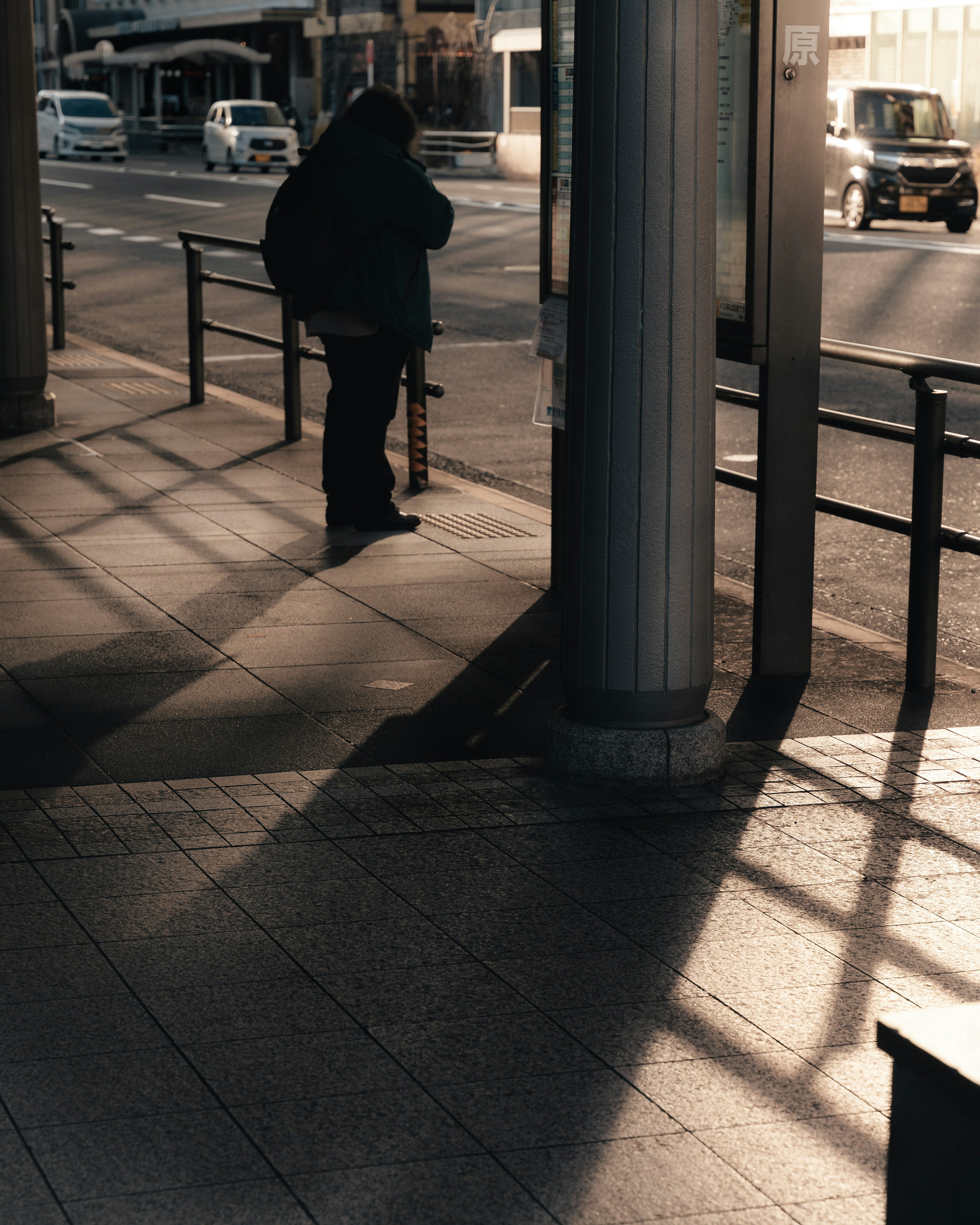 Silhouette of a person holding an umbrella at a bus stop with long shadows