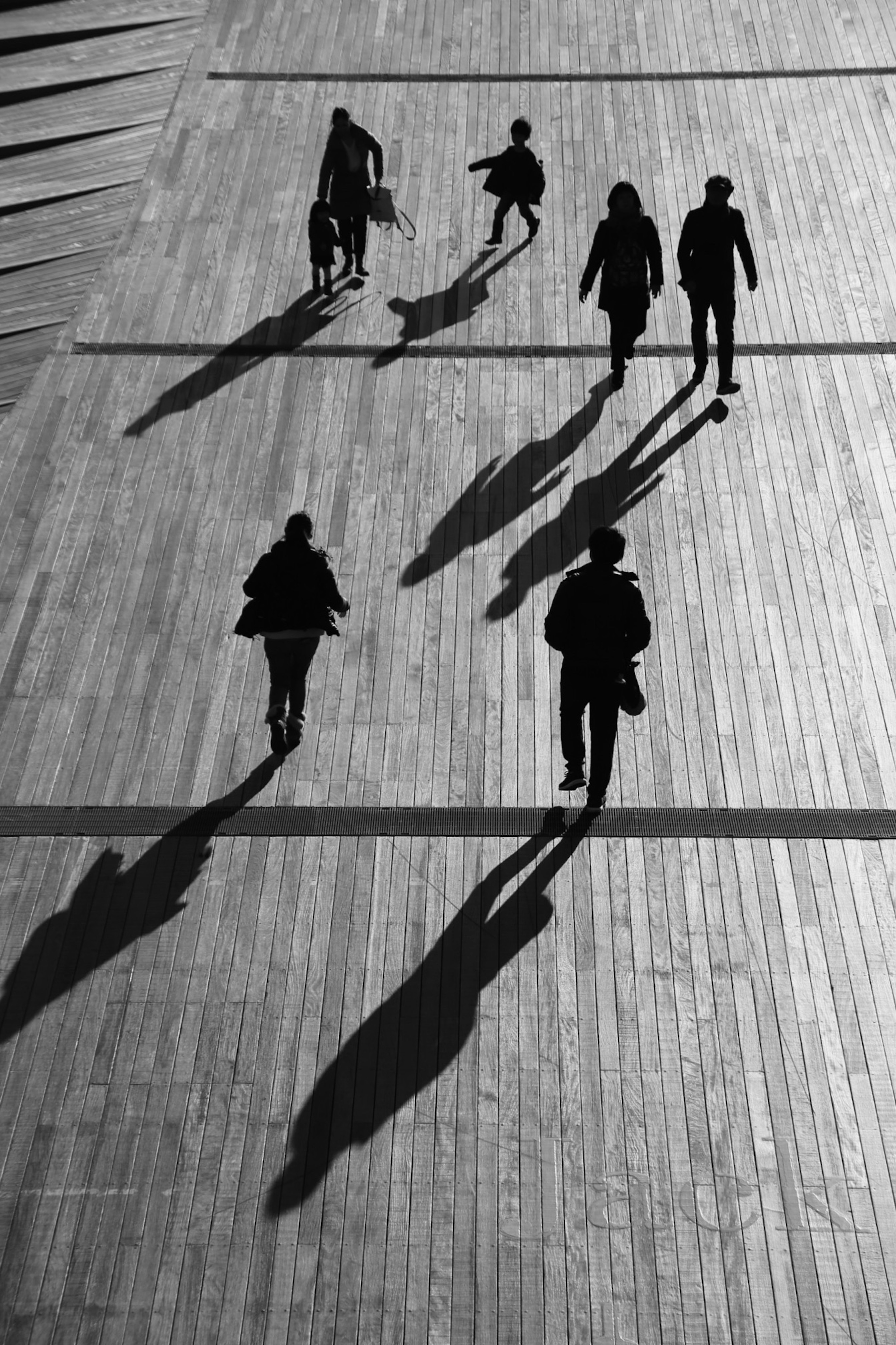 Silhouettes de personnes marchant sur un sol en bois avec de longues ombres