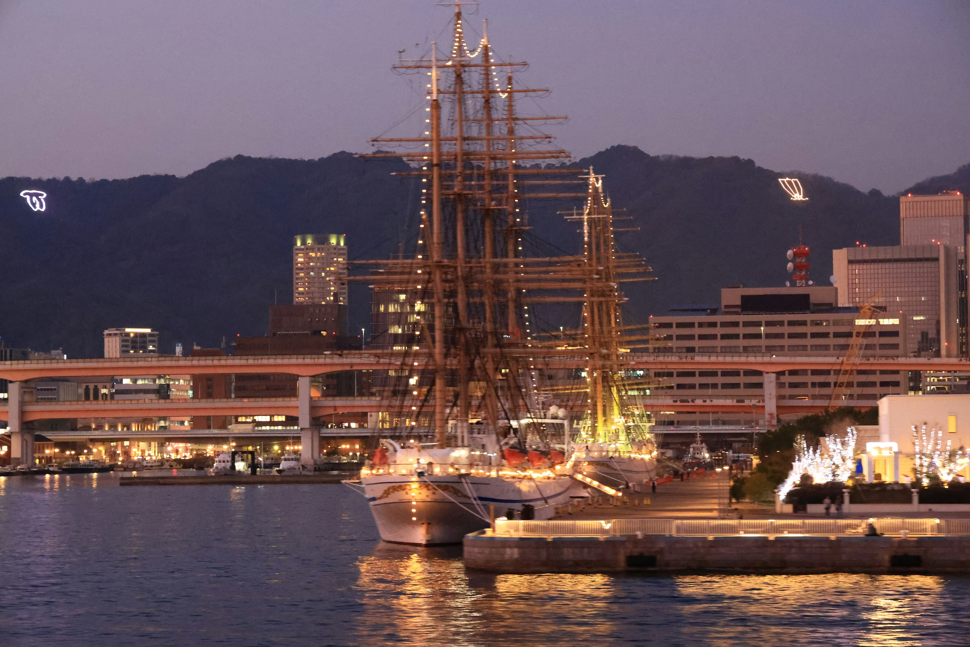 Beautiful sailing ship docked in a harbor at night with mountains in the background