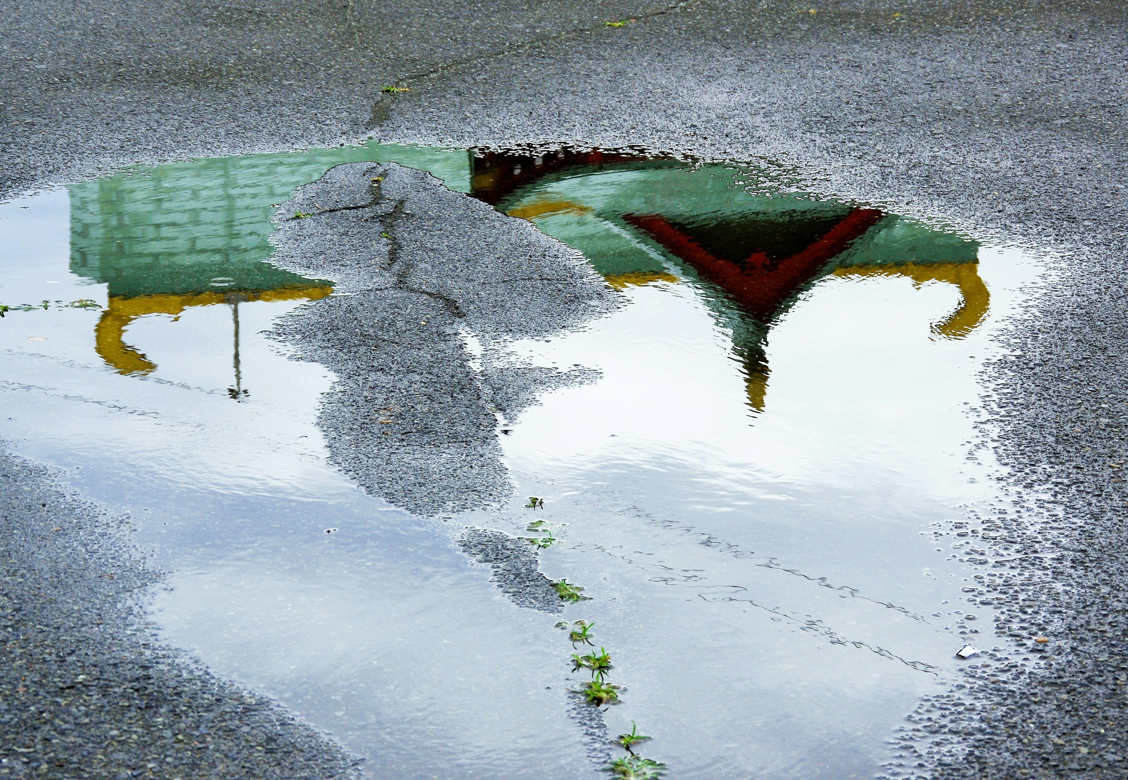 Reflection of a green bench and red triangular pattern in a puddle