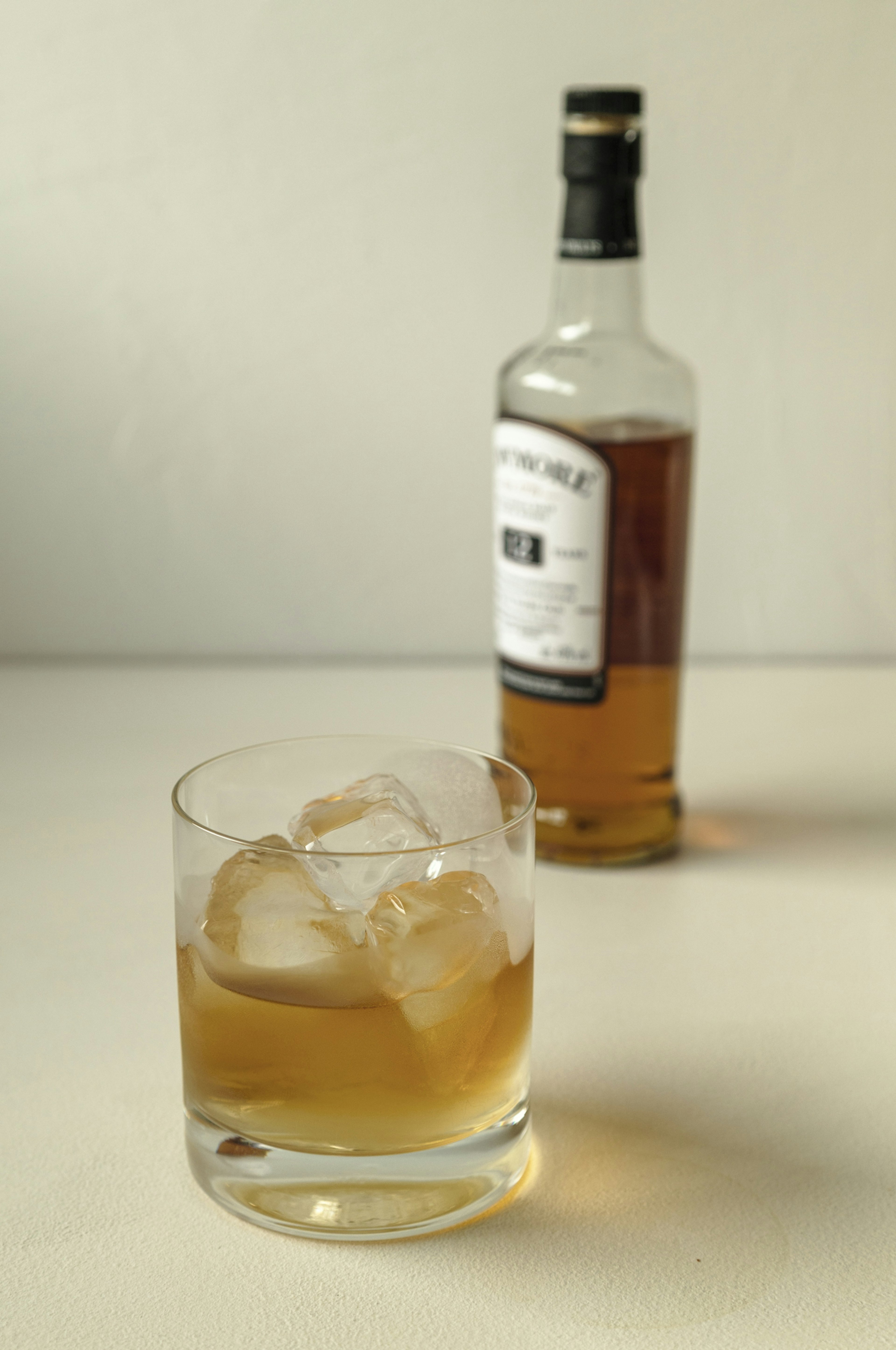 Vaso de whisky con hielo y una botella de whisky al fondo