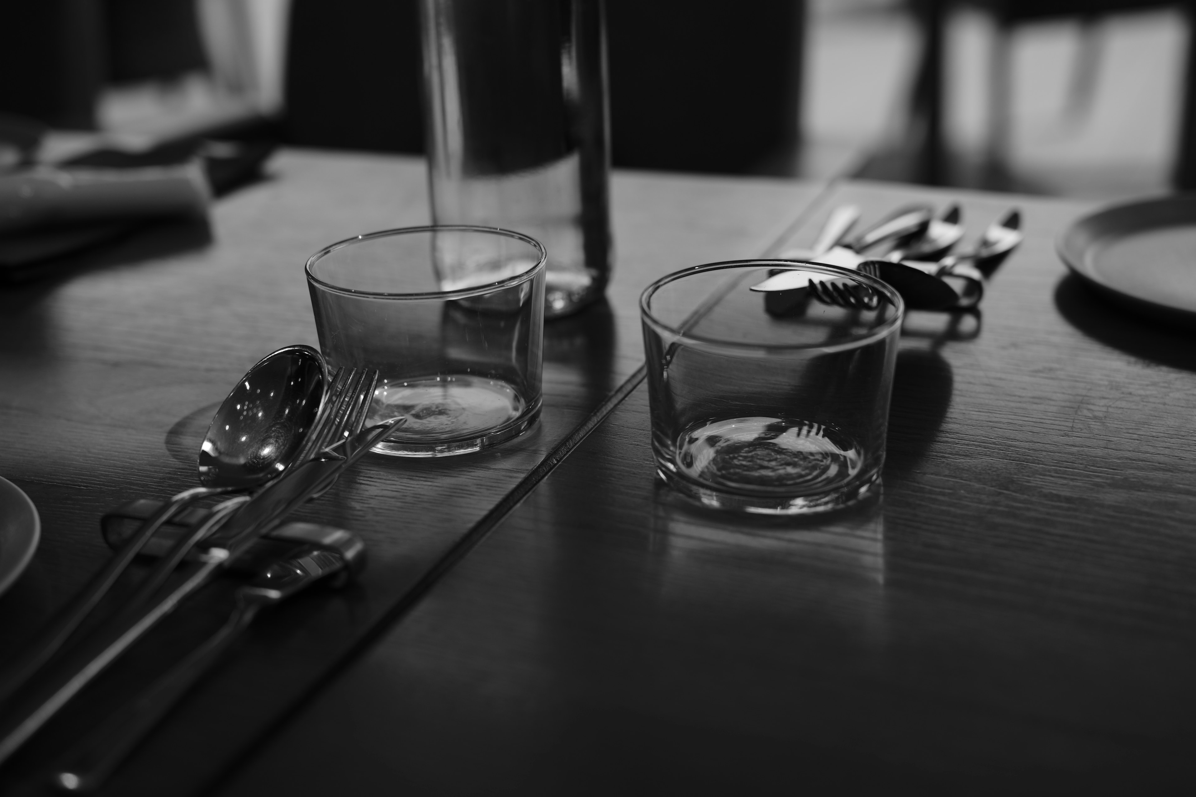 Black and white image of glass cups and cutlery on a table