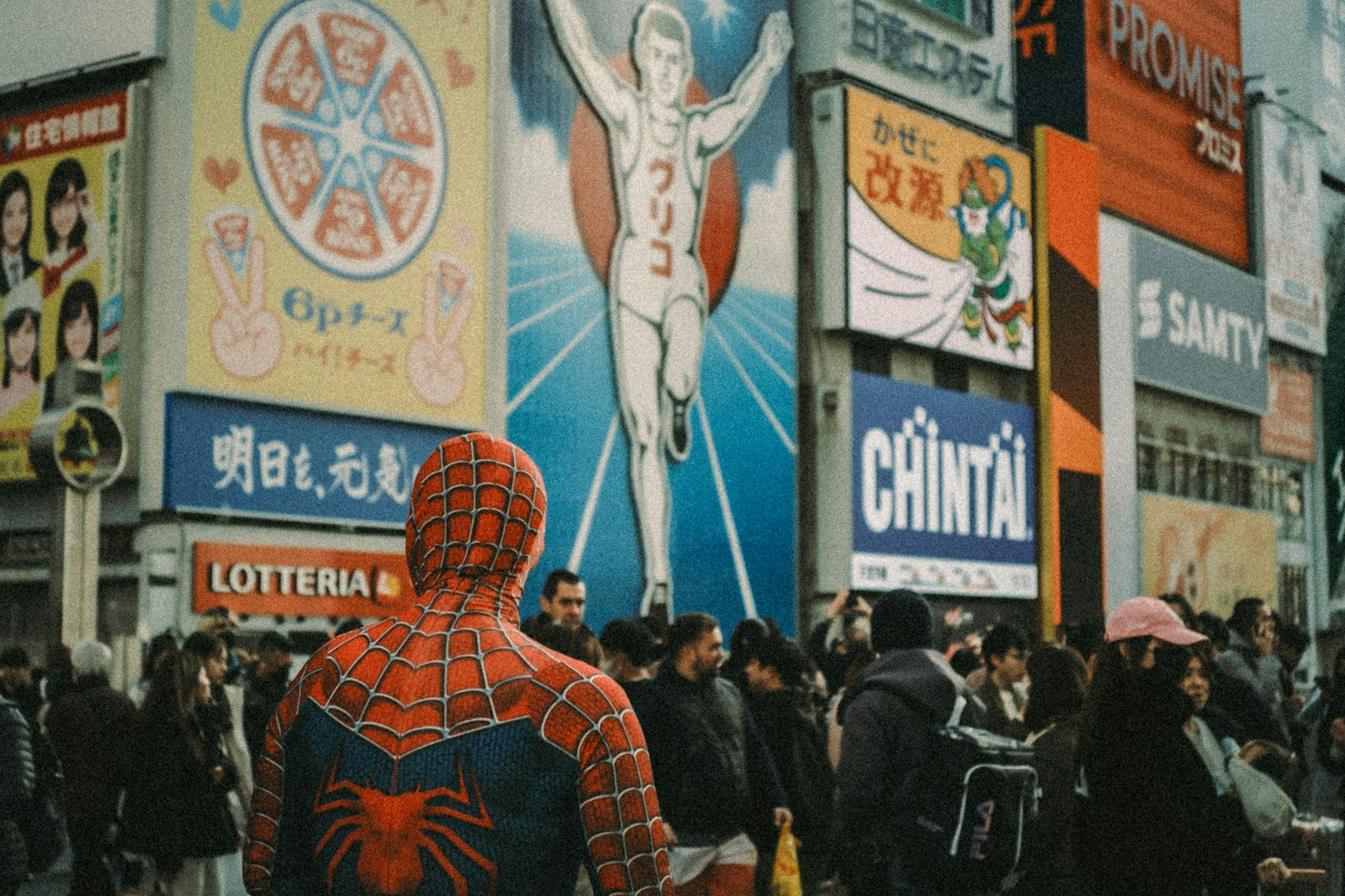 Persona in costume di Spider-Man che si trova di fronte a pubblicità vivaci