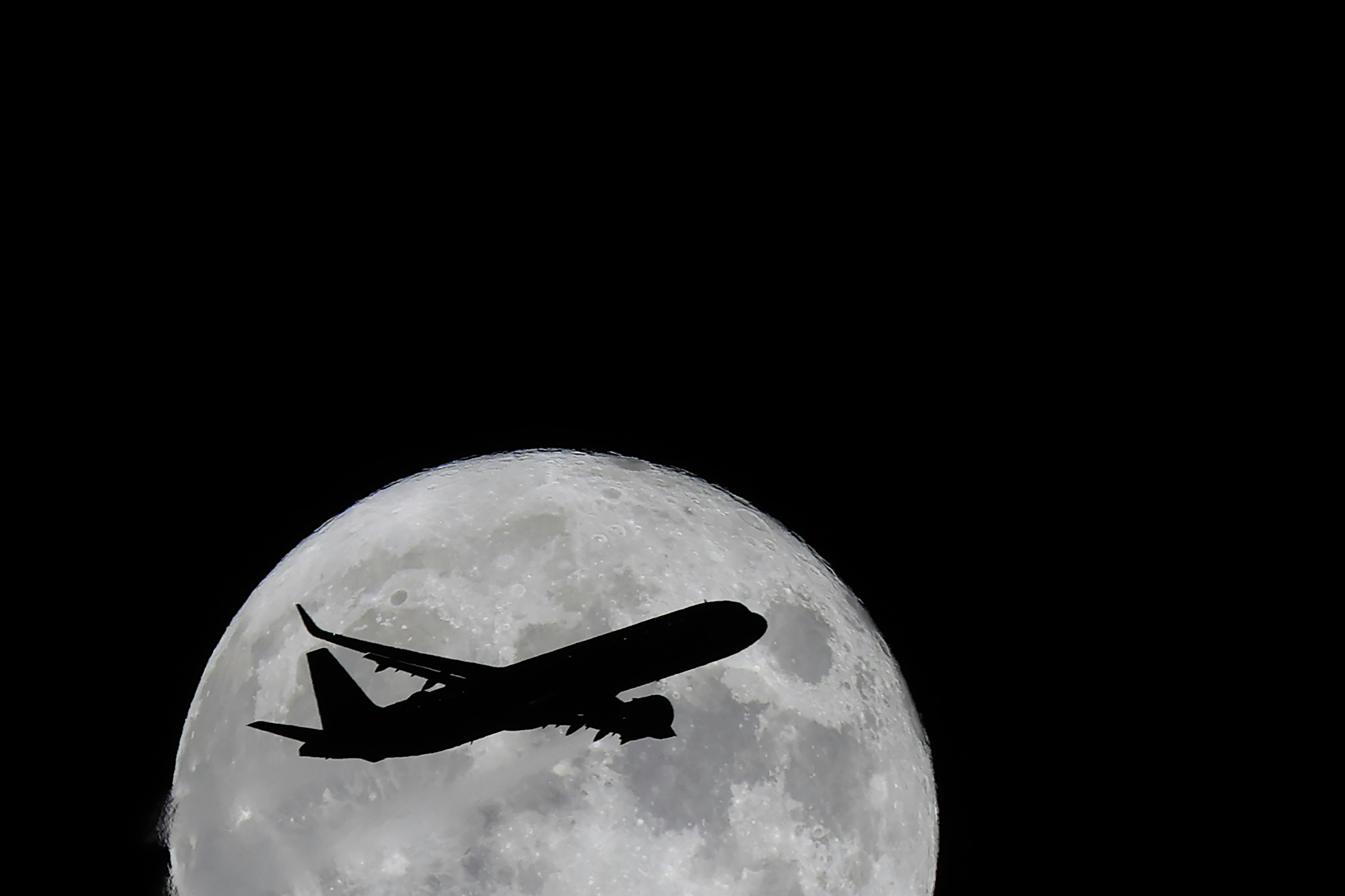 Silhouette di un aereo che vola davanti a una luna piena