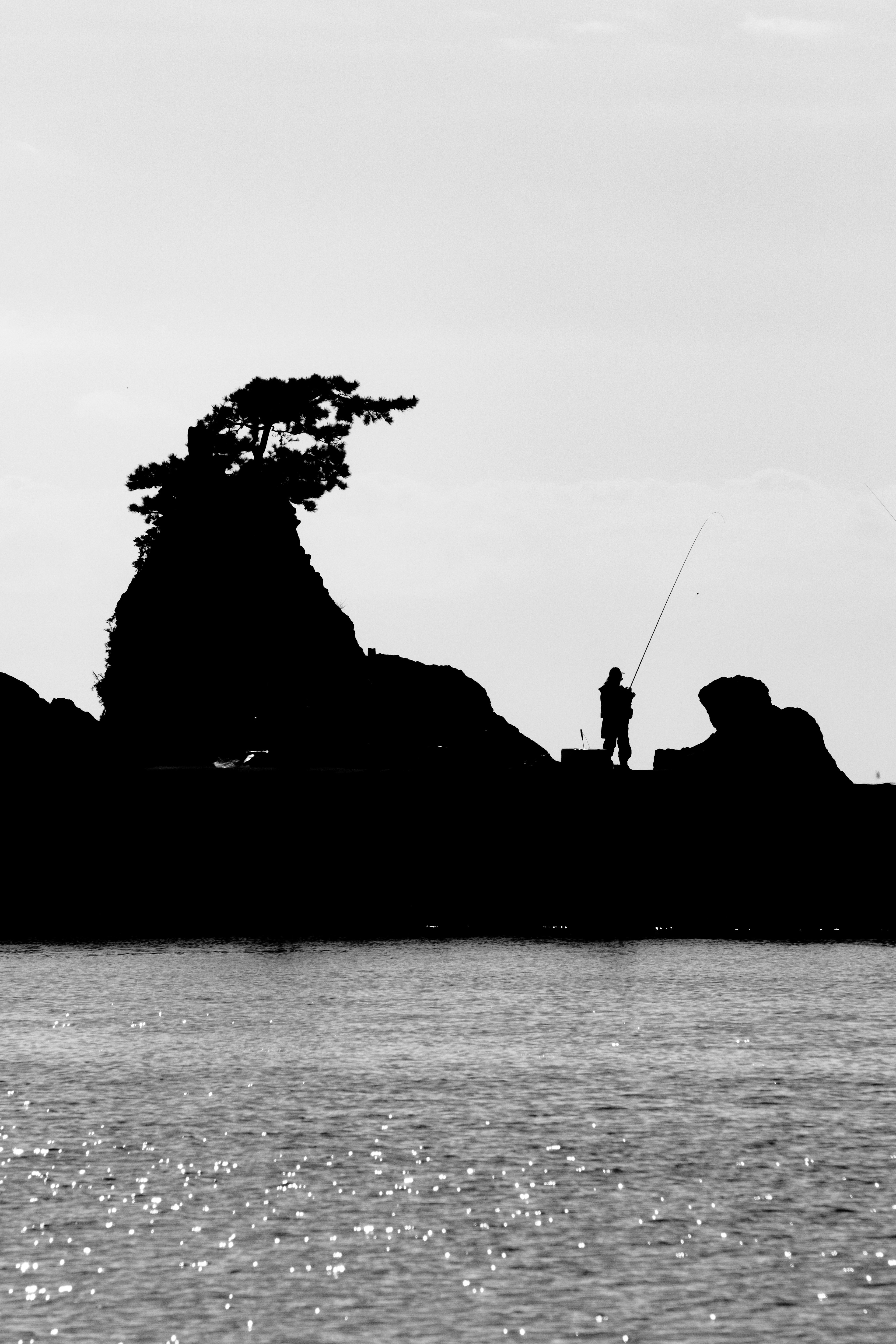 Silhouette di un pescatore e rocce in contrasto bianco e nero